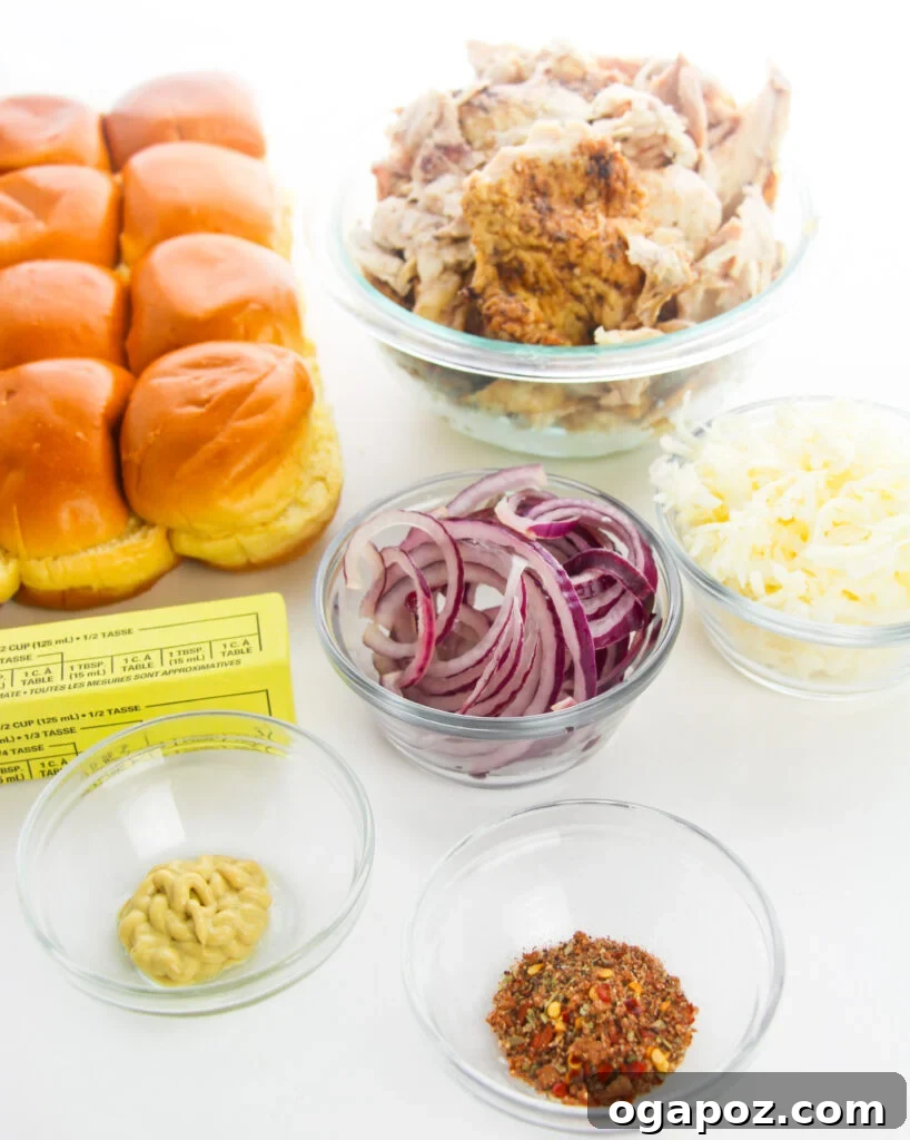 Effortless Chicken Sliders 5 All the fresh ingredients for Easy Chicken Sliders laid out on a wooden board: shredded chicken, cheese, red onion, slider buns, butter, Dijon mustard, and various spices