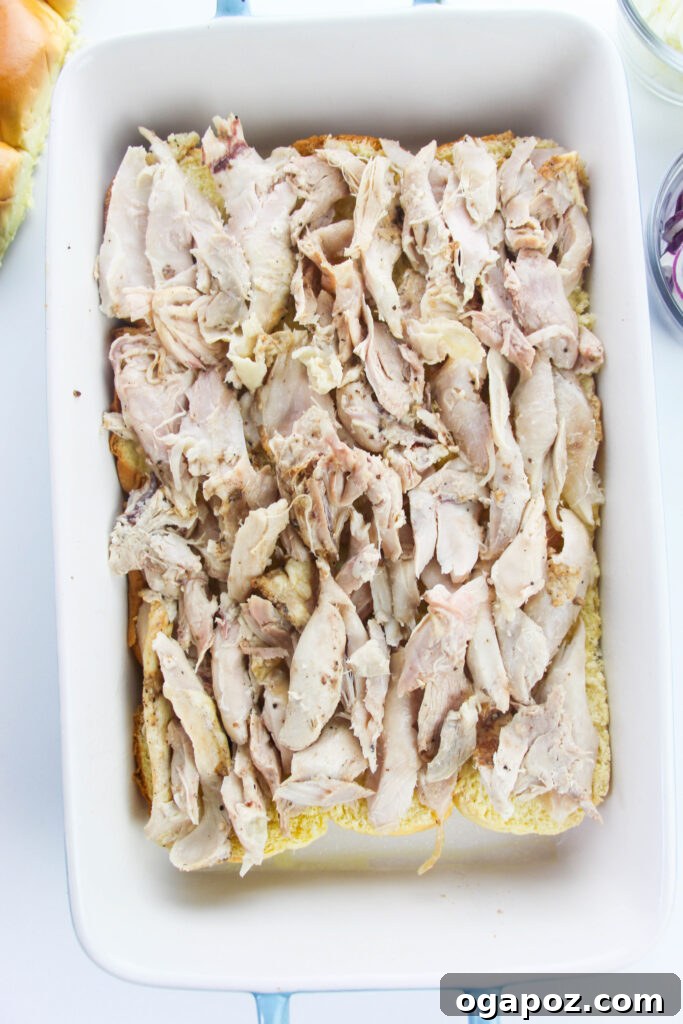 Effortless Chicken Sliders 8 Shredded chicken spread evenly over the bottom layer of slider buns in a baking dish.