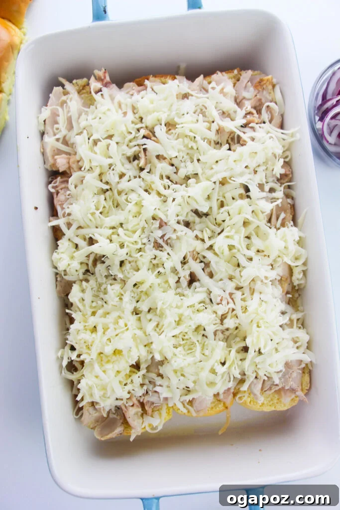 Effortless Chicken Sliders 9 Shredded cheese spread over the chicken layer on the slider buns in a baking dish.