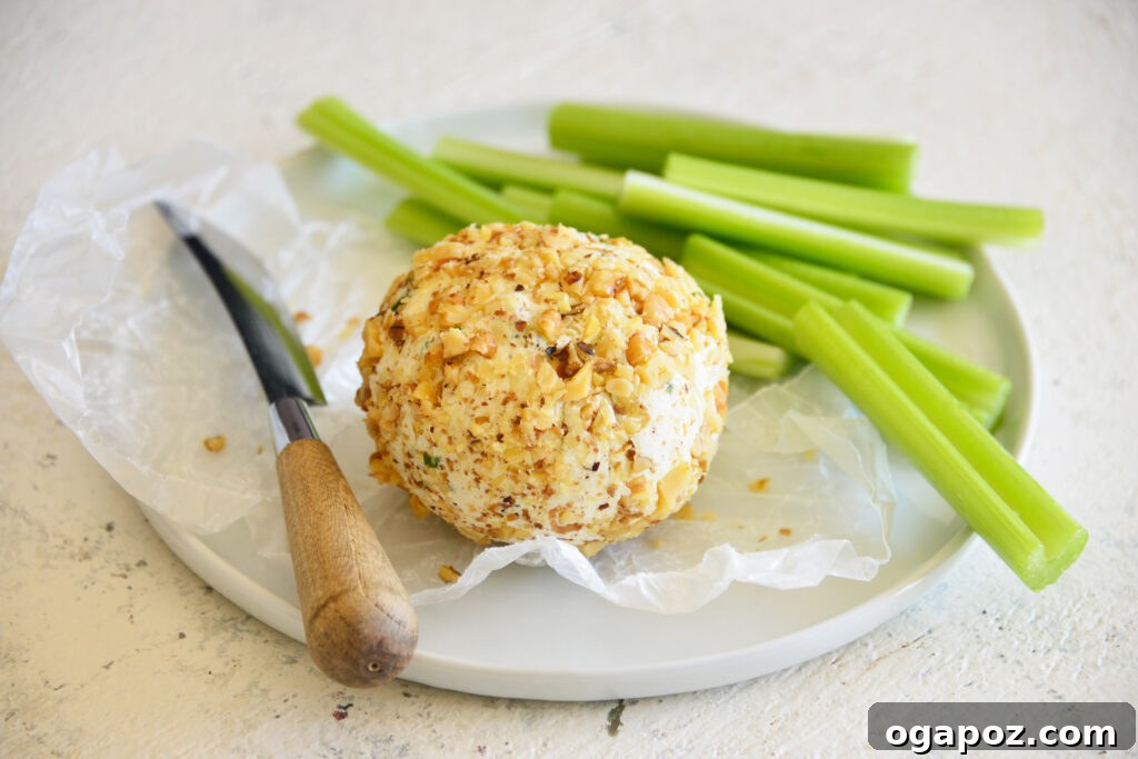 Your Guide to an Irresistible Cheese Ball 3 A freshly made cheese ball, ready to be served, with a small knife indicating its creamy texture, placed on a white background.