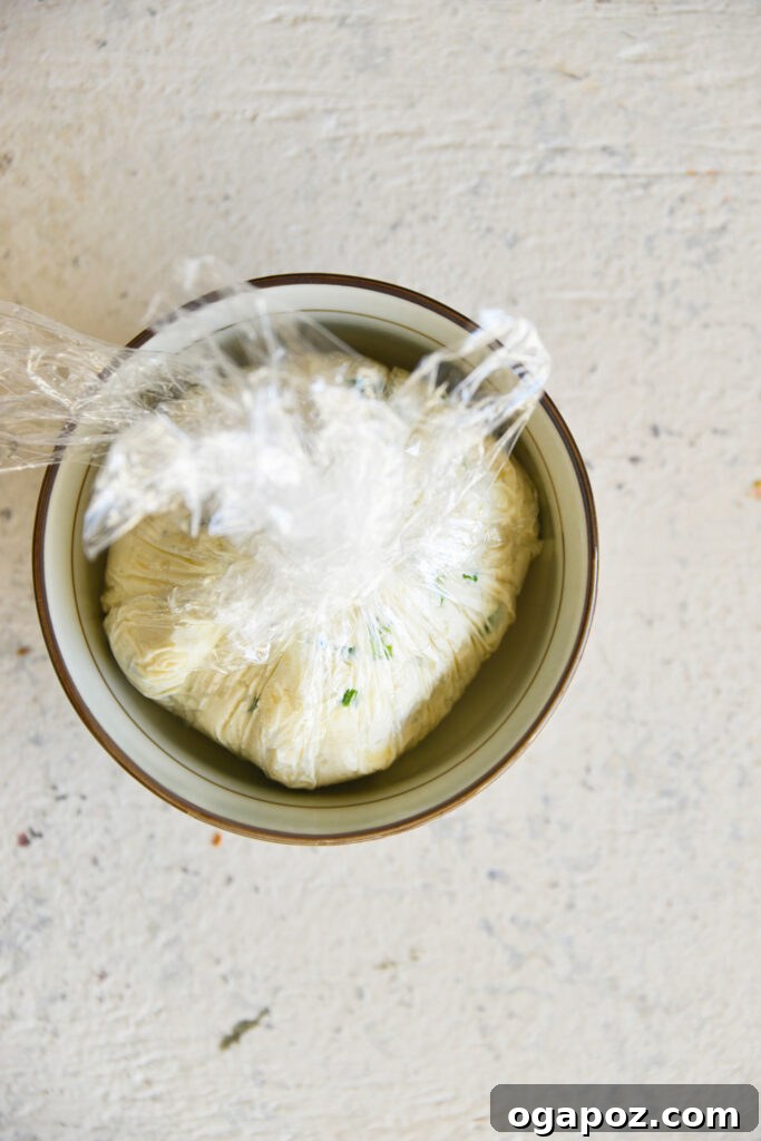 Your Guide to an Irresistible Cheese Ball 7 A cheese ball wrapped in plastic wrap, placed inside a small bowl for chilling in the refrigerator, emphasizing preparation ahead of time.