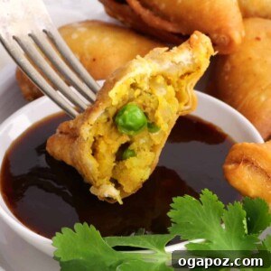 Close-up of a perfectly fried potato samosa with a bite taken out, dipped in chutney.