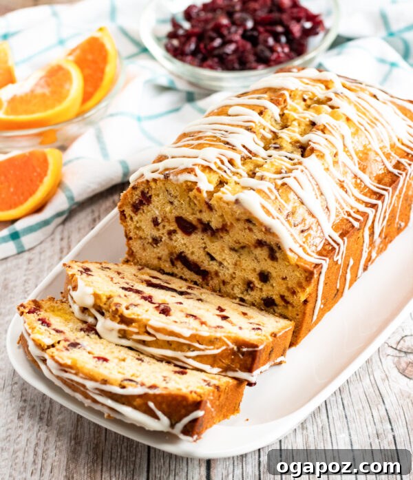 Sweet and Tart Cranberry Loaf 2 A freshly baked loaf of Cranberry Orange Bread on a wooden board, garnished with fresh cranberries and orange slices.