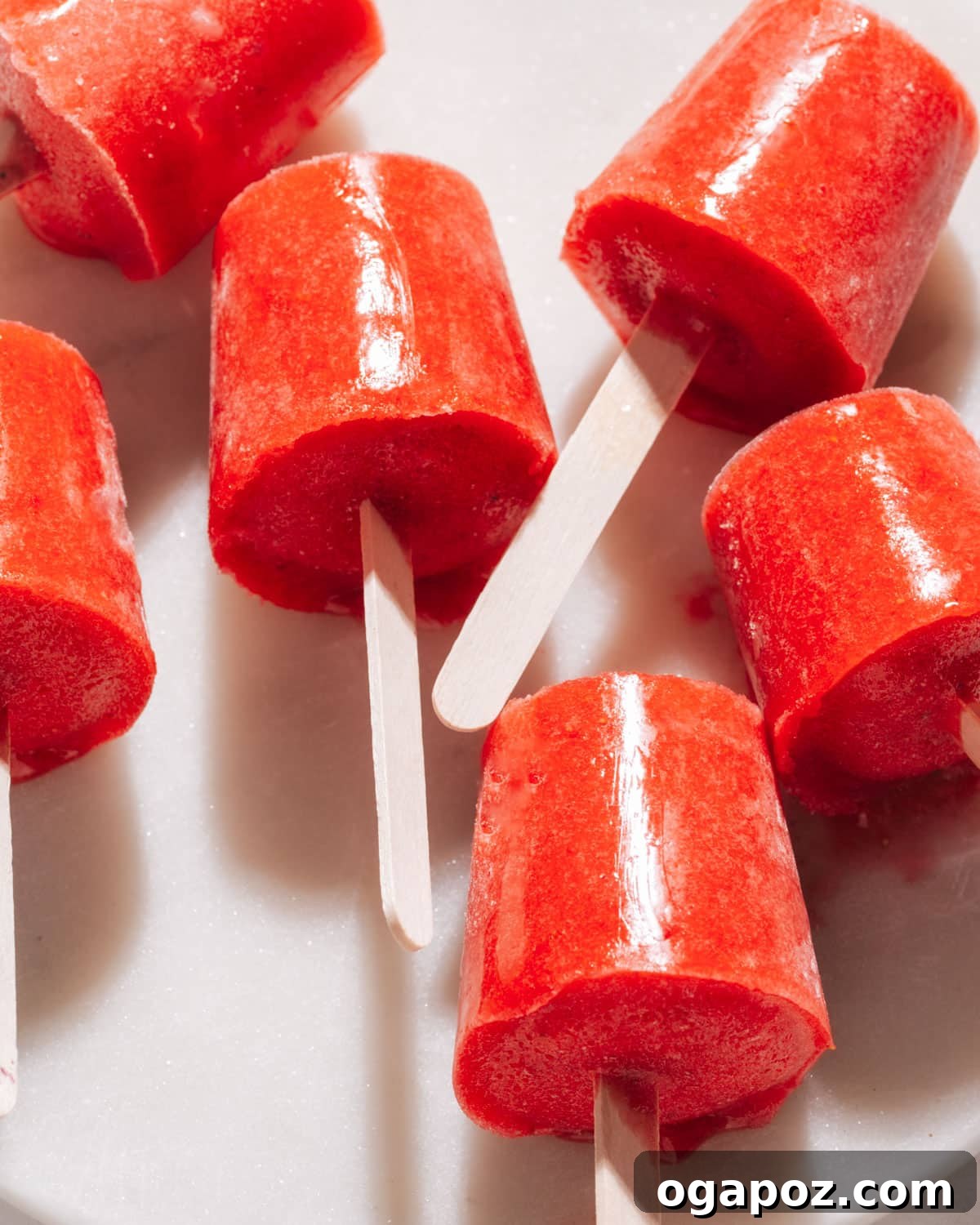 Three homemade strawberry popsicles arranged neatly on a white plate, showcasing their smooth texture and vibrant red hue.