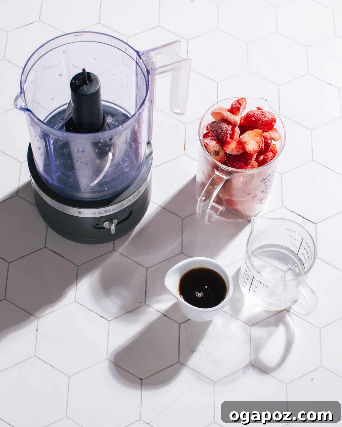 A flat lay photograph displaying the simple ingredients required for strawberry popsicles: fresh strawberries, a jar of honey, and a glass of water.