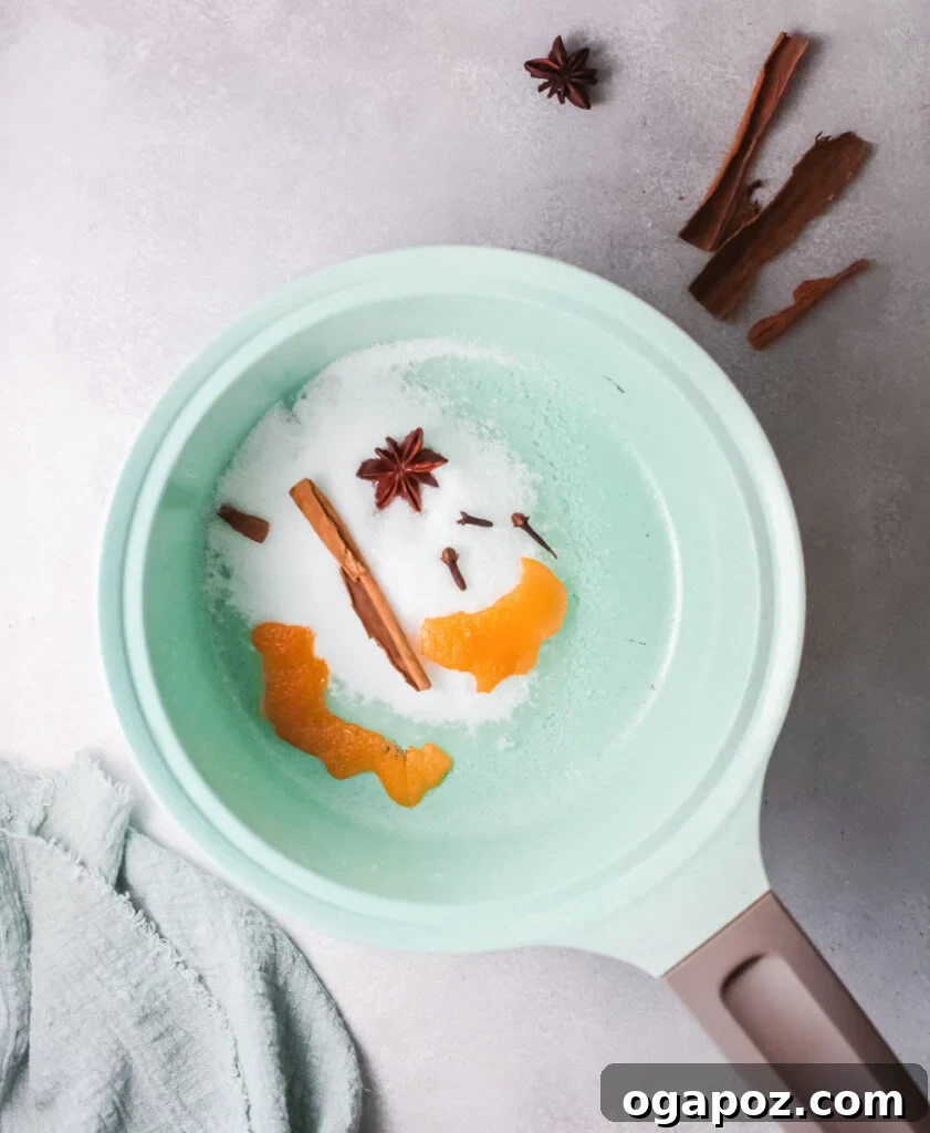 Simple syrup mixture for Cranberry Wine Spritzer simmering in a pot with spices and orange peels