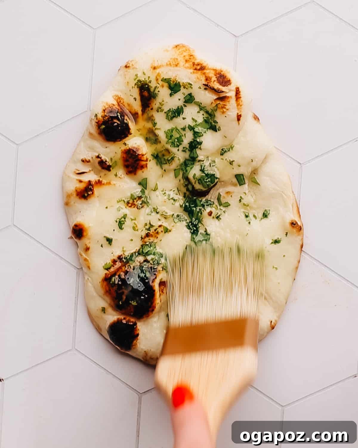 Pillowy Soft, Perfectly Stretchy Garlic Naan 8 A freshly cooked garlic naan being brushed generously with melted garlic butter and cilantro.