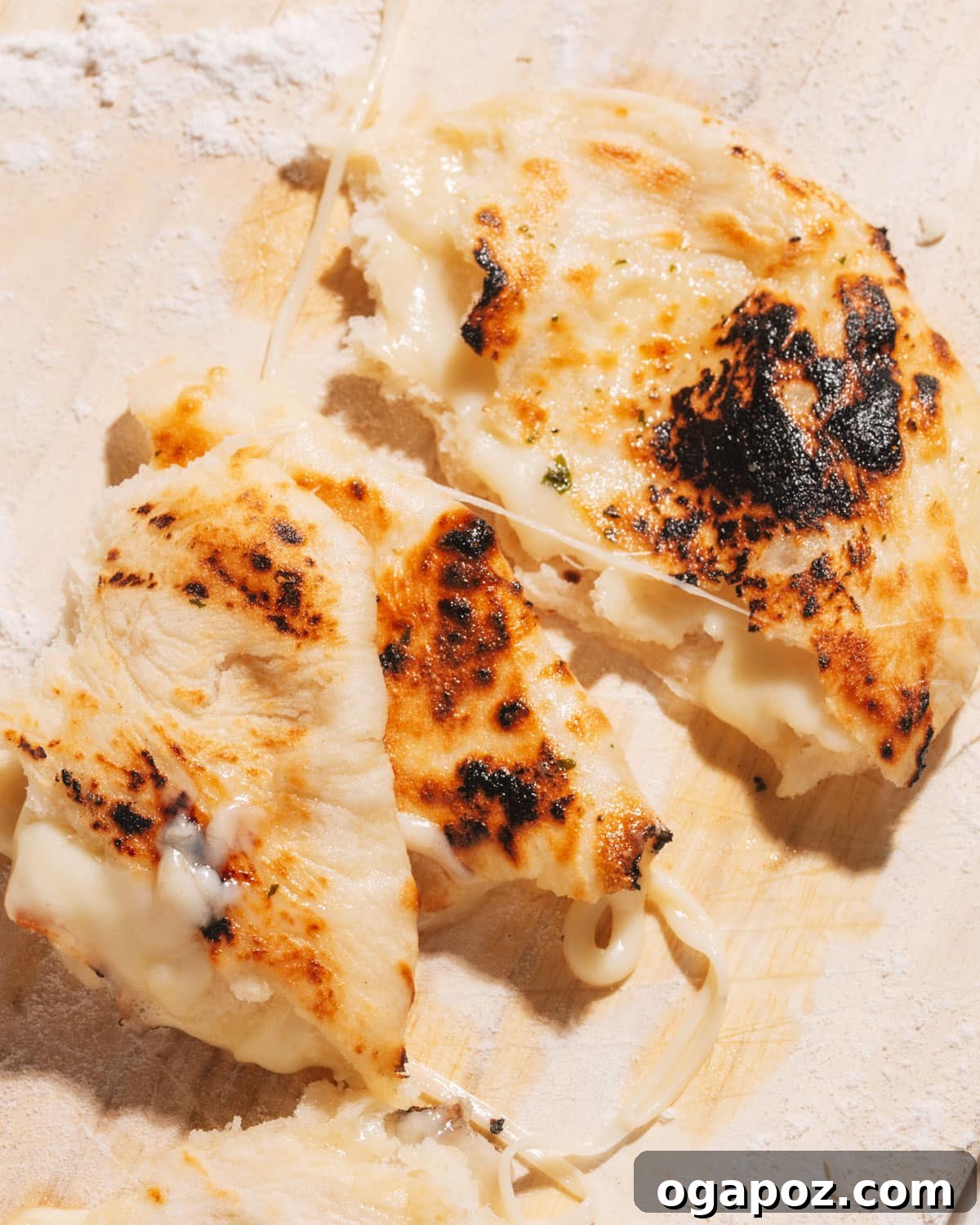 Gooey Cheese Naan 2 Golden brown cheese naan bread on a wooden cutting board, with warm, gooey cheese gently melting out from a tear.