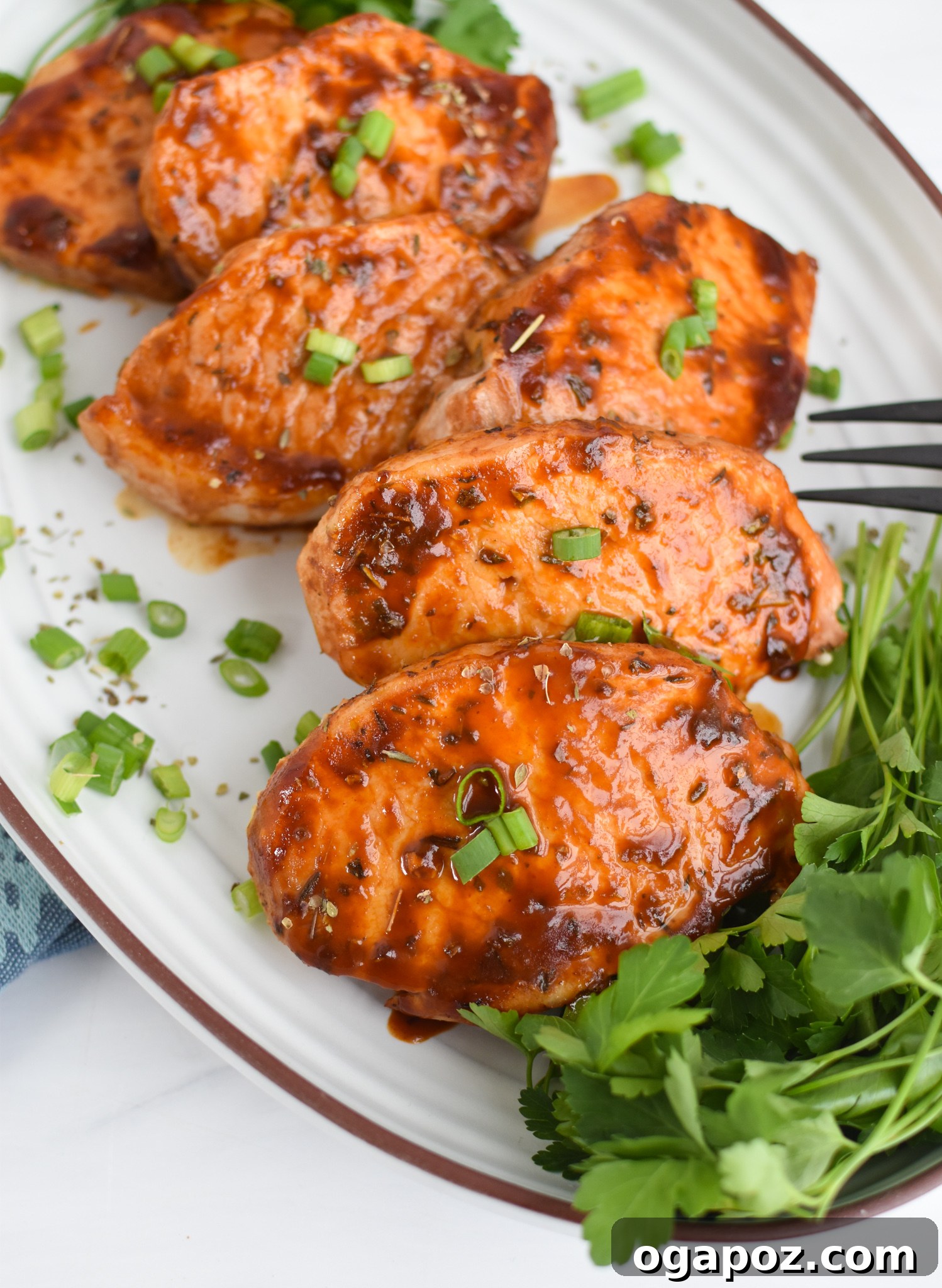 Succulent Oven Baked BBQ Pork Chops 2 Perfectly cooked BBQ Baked Pork Chops arranged on a white platter, garnished with fresh herbs.