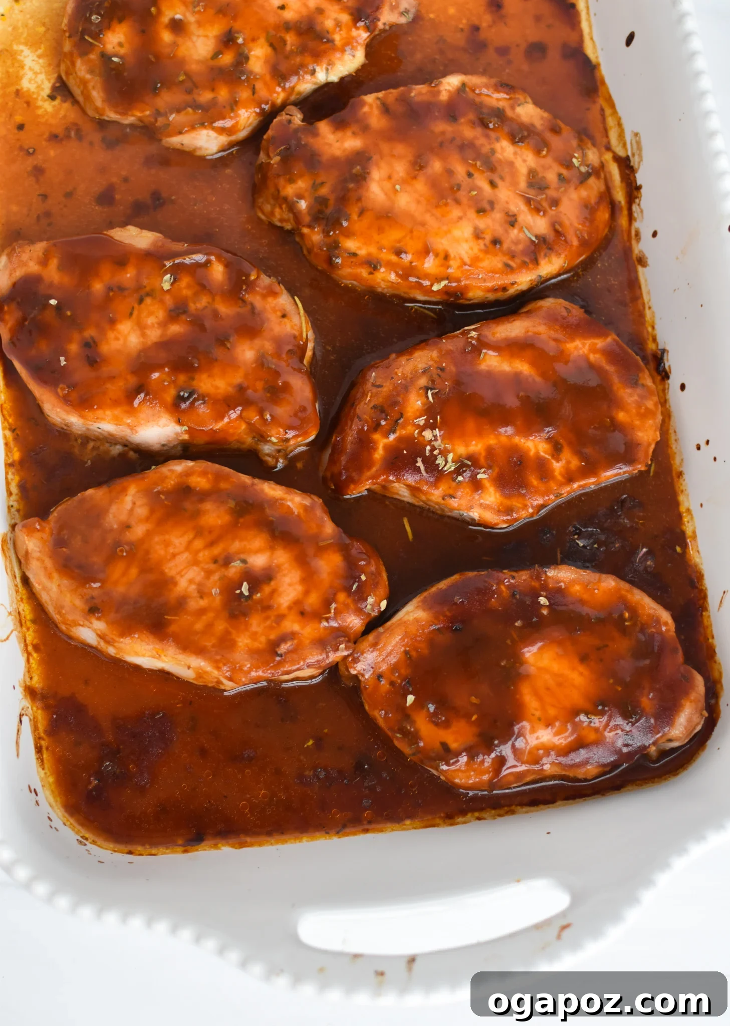Succulent Oven Baked BBQ Pork Chops 7 BBQ Baked Pork Chops cooking in a baking dish, glazed with sauce.