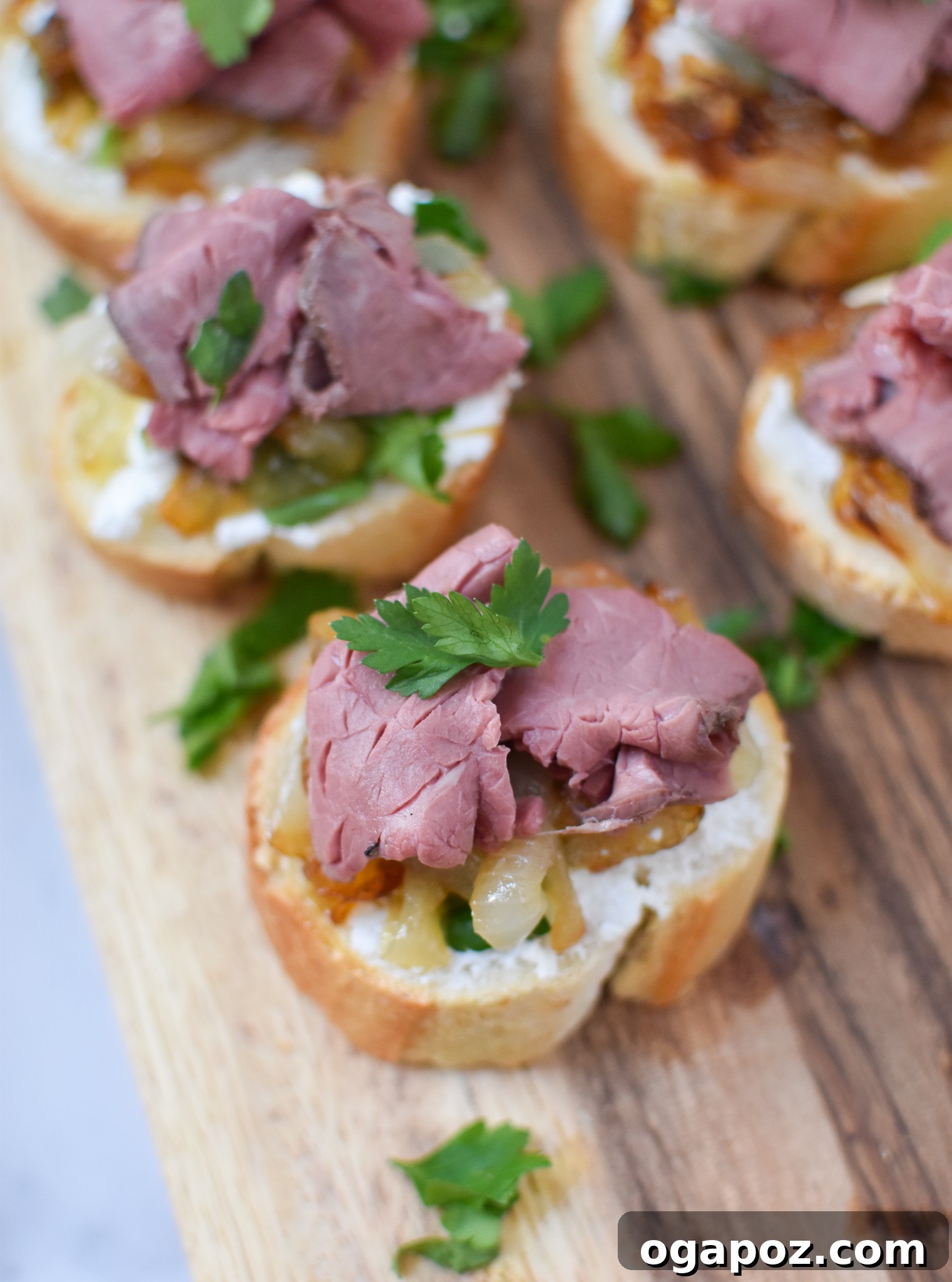 Gourmet Beef Crostini with Sweet Onion Jam 4 Three prepared Beef Crostini with Caramelized Onion and Goat Cheese presented on a white plate, garnished with fresh herbs.