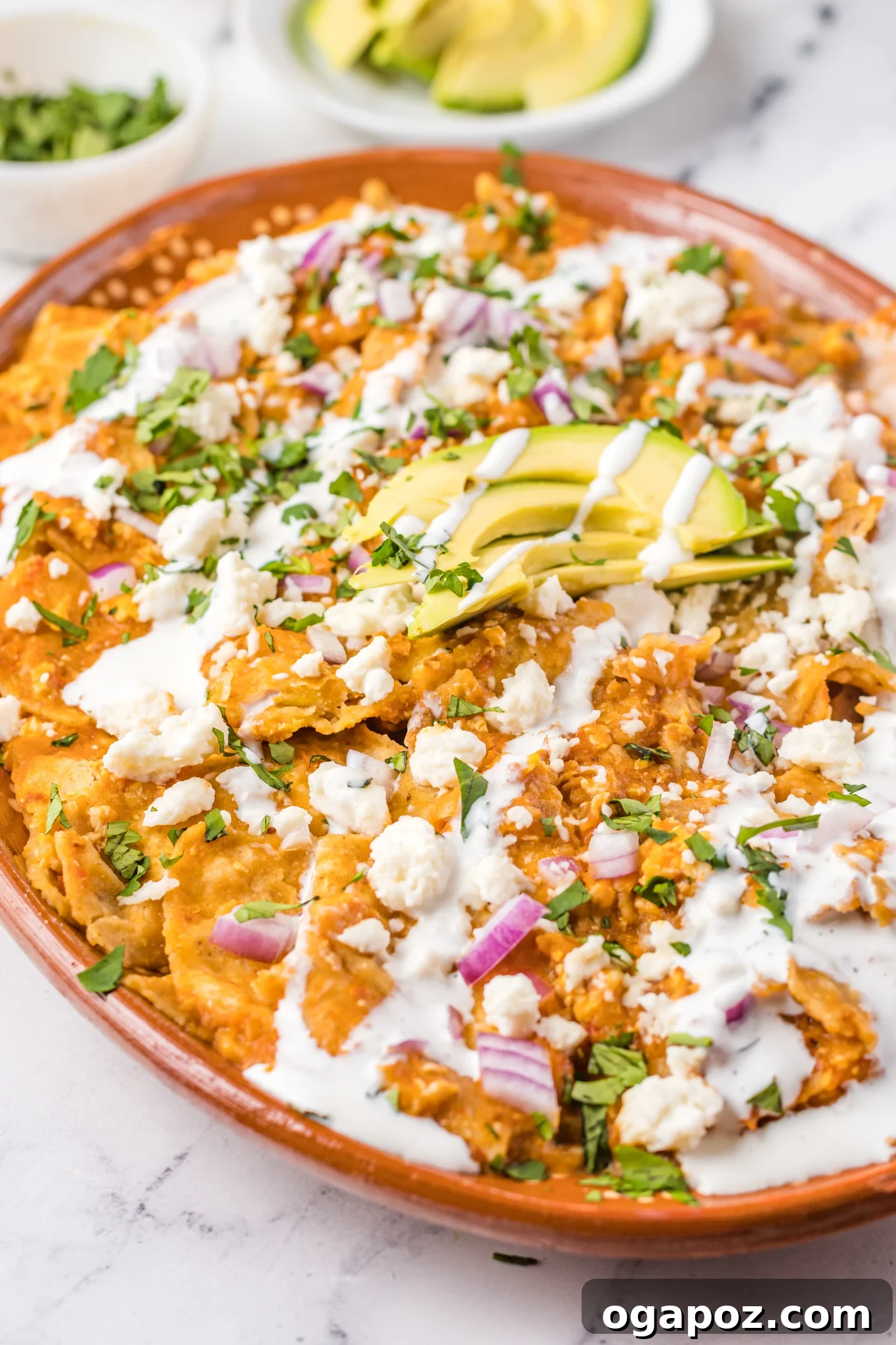 Authentic Mexican Chilaquiles Rojos 2 Chilaquiles Rojos Recipe served on a platter with avocado slices, crumbled queso fresco, and fresh cilantro.