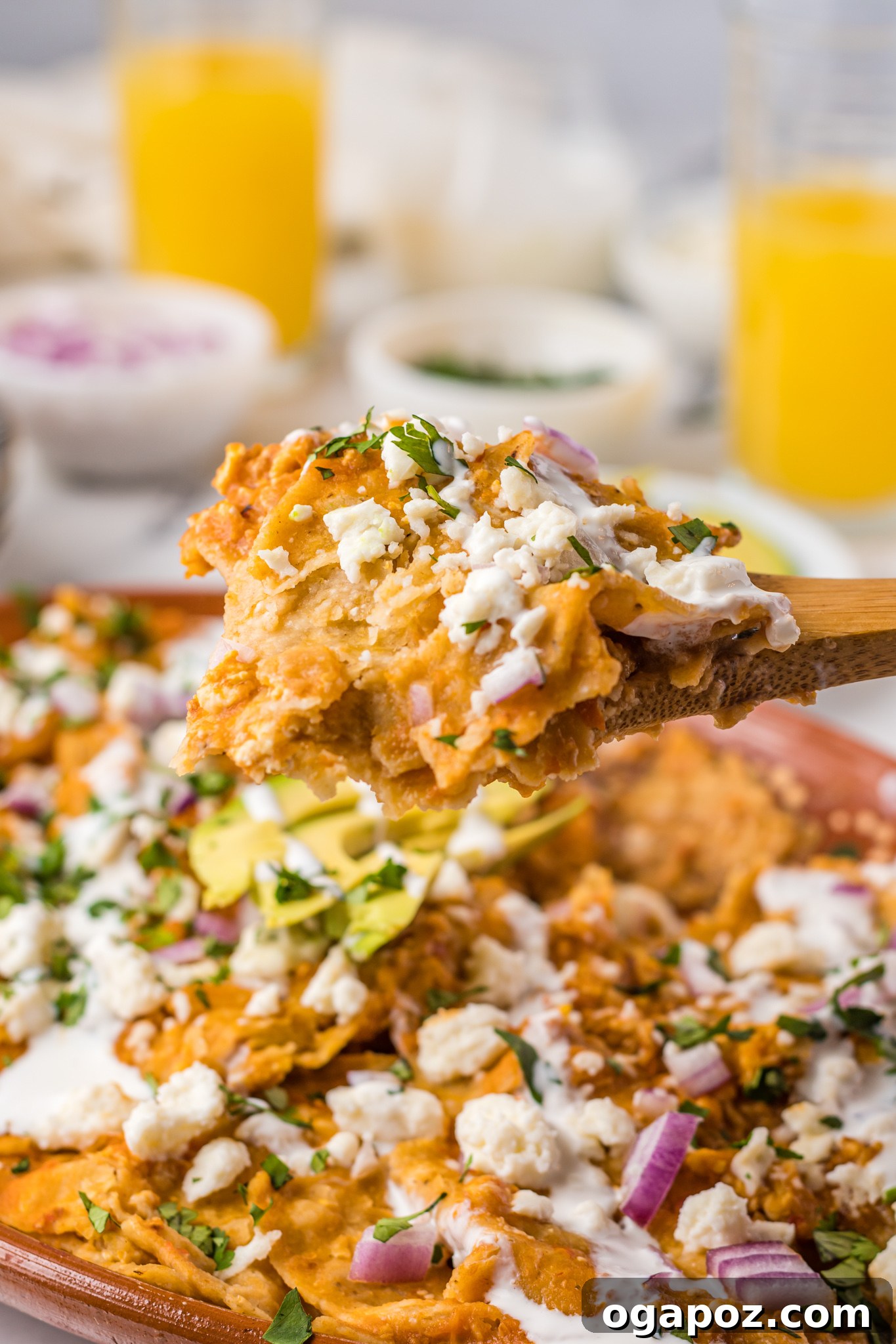 Authentic Mexican Chilaquiles Rojos 11 A wooden spoon lifting a spoonful of Chilaquiles Rojos, showing the saucy chips and melted cheese.