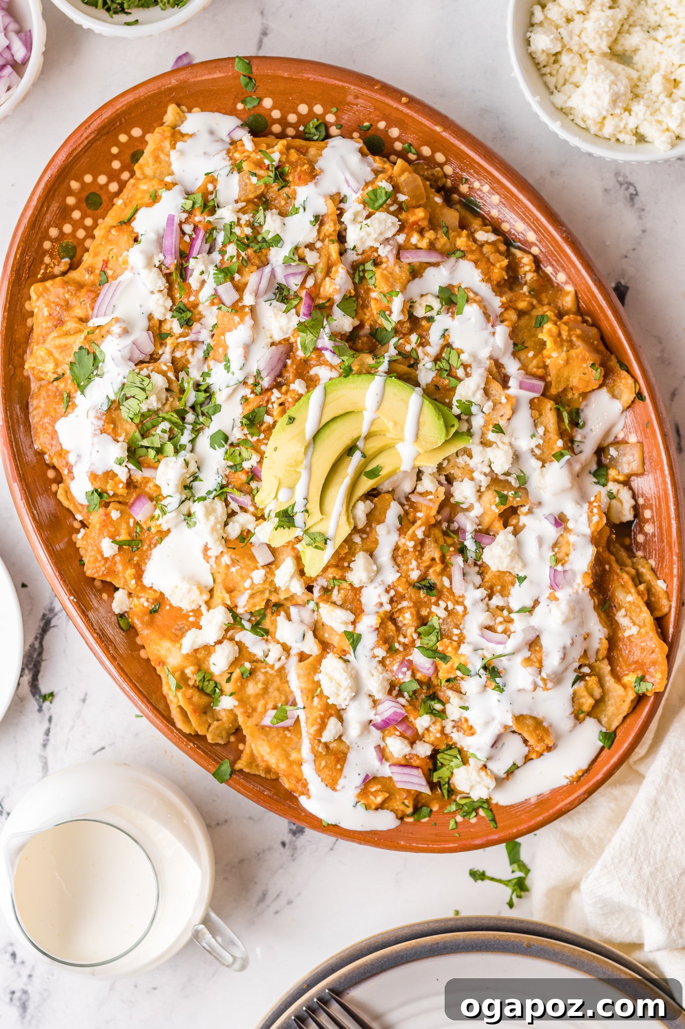 Authentic Mexican Chilaquiles Rojos 4 A large platter filled with Chilaquiles Rojos, generously topped with slices of avocado, a drizzle of Mexican crema, and crumbled queso fresco.