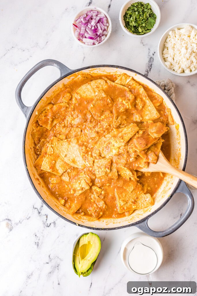 Authentic Mexican Chilaquiles Rojos 8 The red sauce being poured over tortilla chips and eggs in a skillet, coating them evenly.