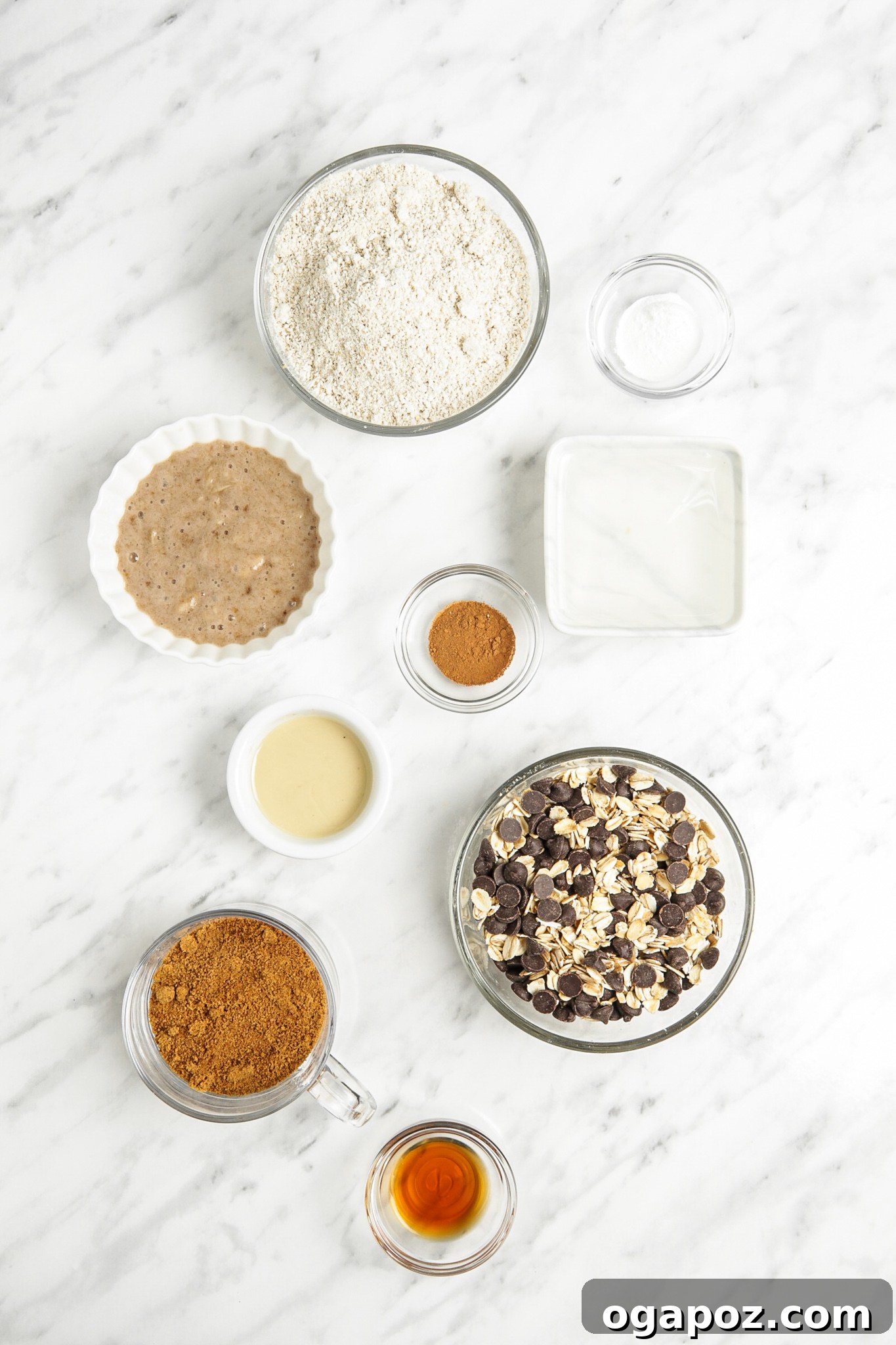 Soft-Baked Banana Oatmeal Cookies 3 A collection of ingredients for Homemade Banana Oatmeal Cookies, including oat flour, coconut sugar, almond butter, bananas, oats, and chocolate chips, laid out on a kitchen counter.