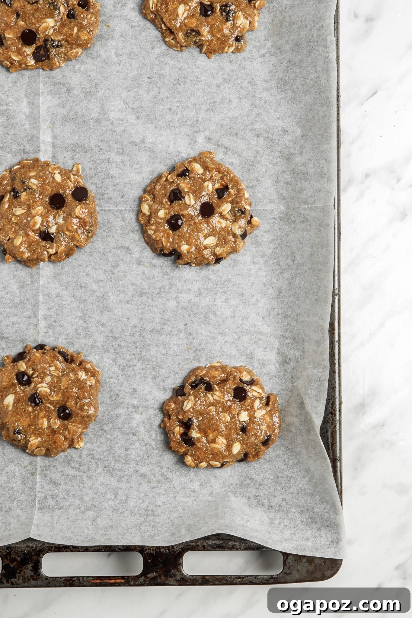 Soft-Baked Banana Oatmeal Cookies 8 Flattened balls of Homemade Banana Oatmeal Cookie dough on a parchment-lined baking sheet, ready for the oven.