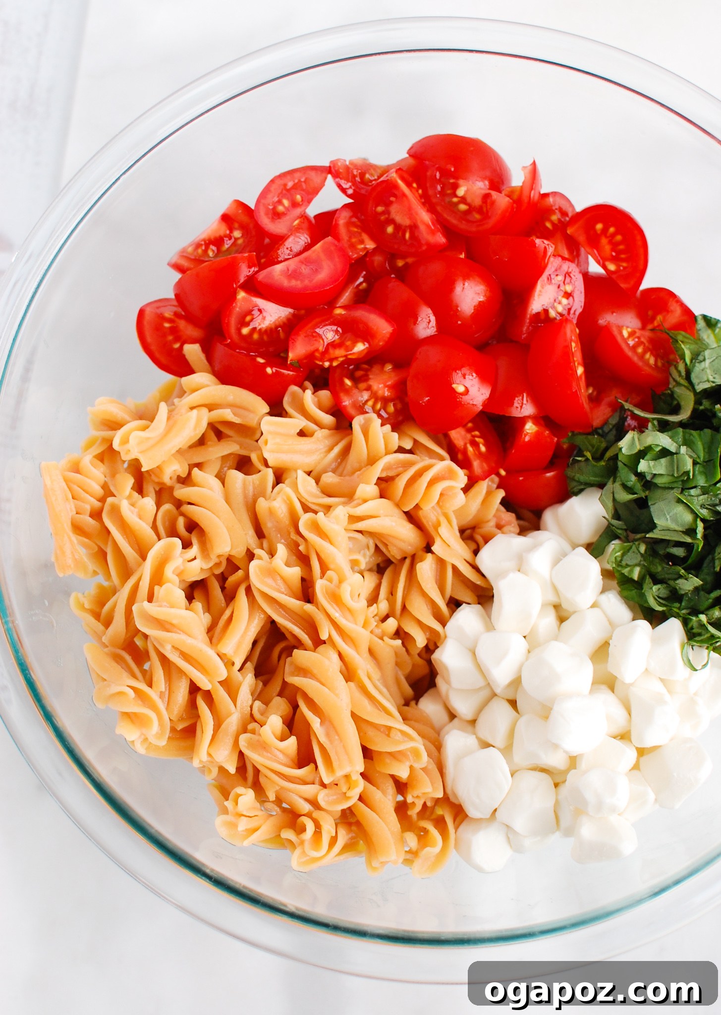 Vibrant Caprese Pasta 3 Fresh ingredients for Caprese Pasta including pearl mozzarella, cherry tomatoes, and fresh basil leaves, arranged in a white bowl.