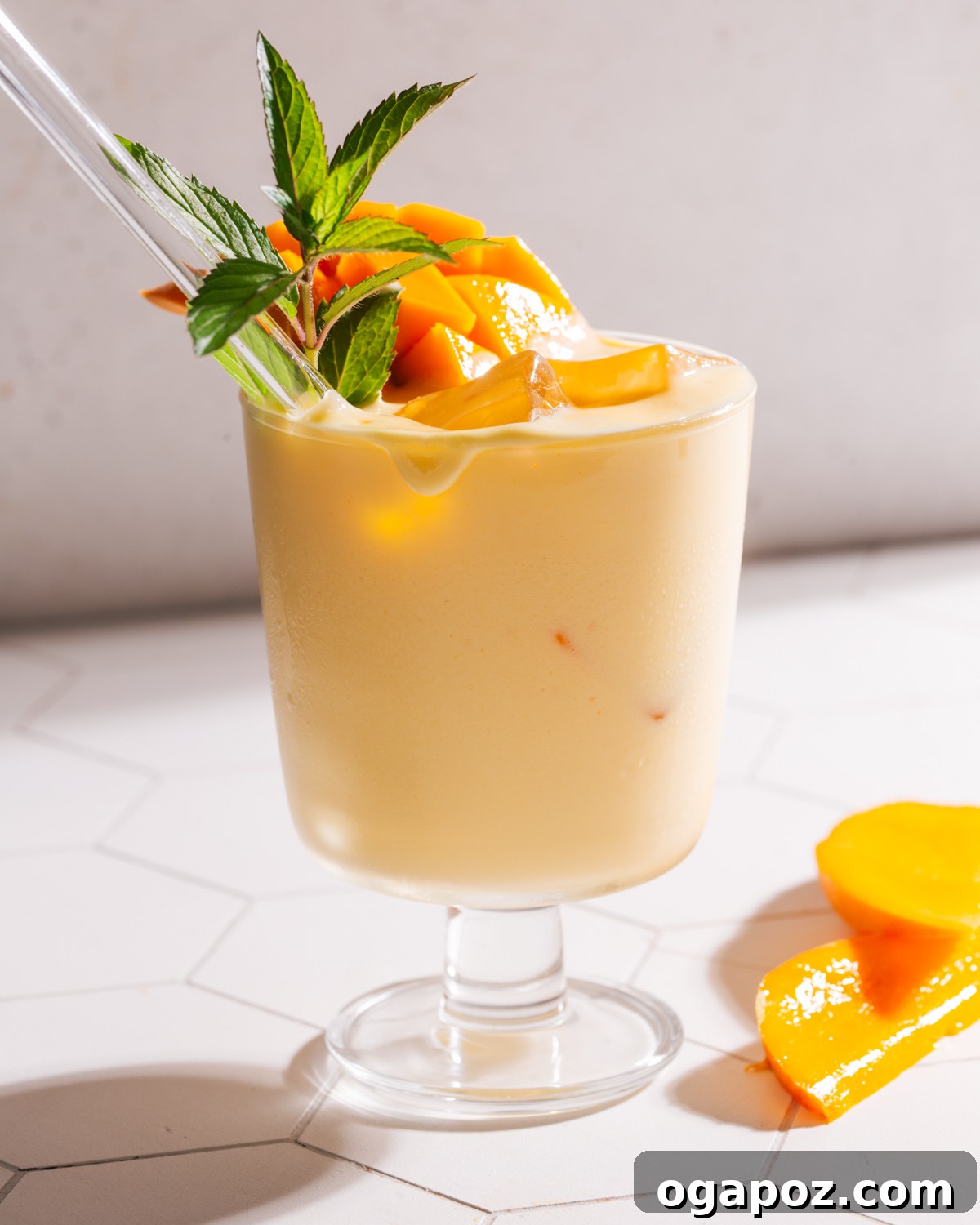 A glass of mango lassi with a straw, garnished with mint leaves and fresh mango slices