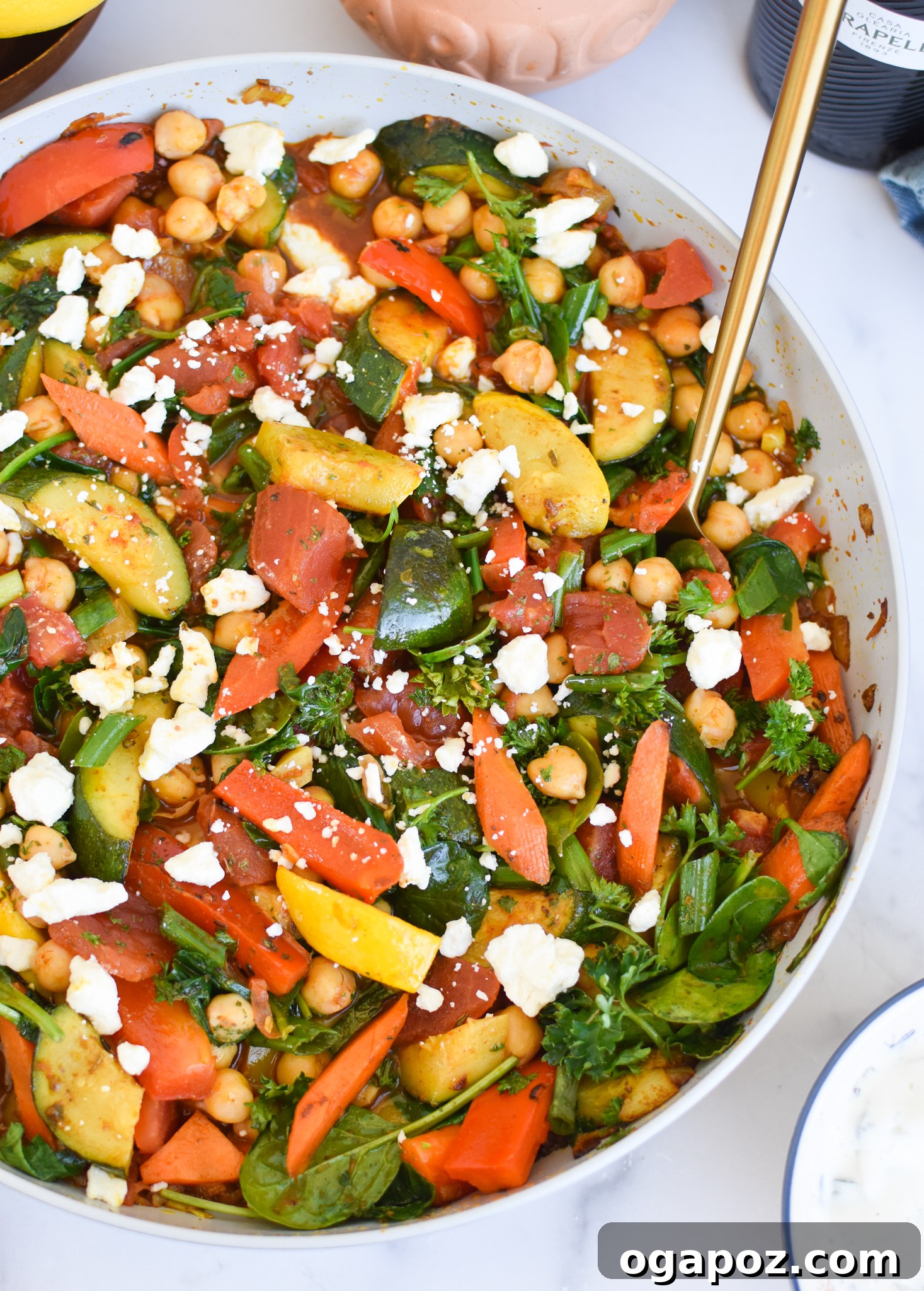 Vibrant Mediterranean Chickpea Skillet 3 Close-up of Mediterranean Chickpea Skillet in a pan with a gold serving spoon, highlighting the rich textures and colors of the ingredients.