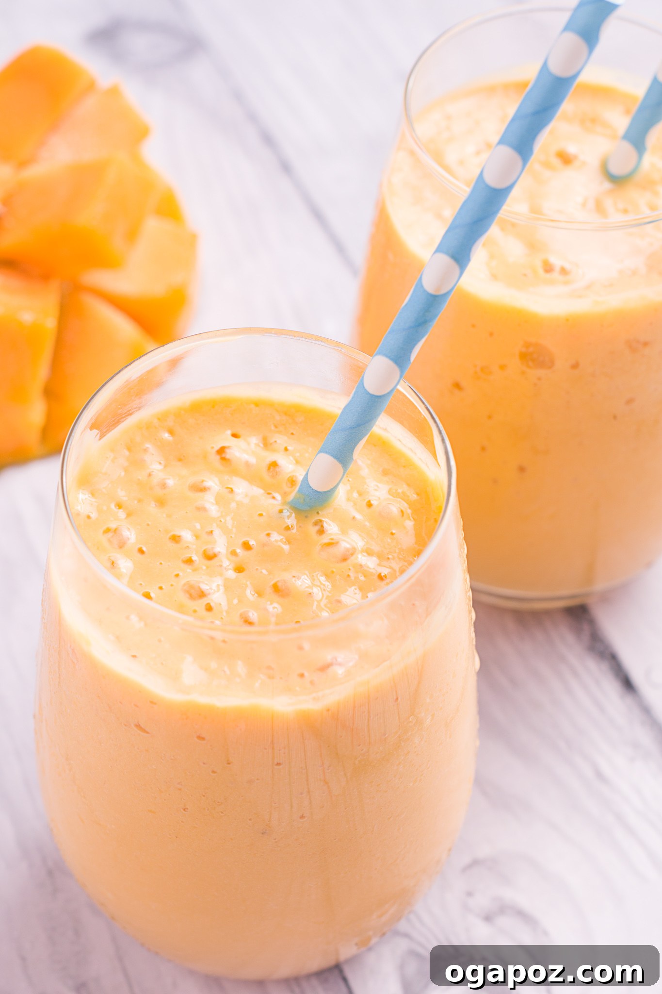 Velvety Mango Lassi 2 Creamy Homemade Mango Lassi in a clear glass with a straw, garnished with fresh mint leaves.