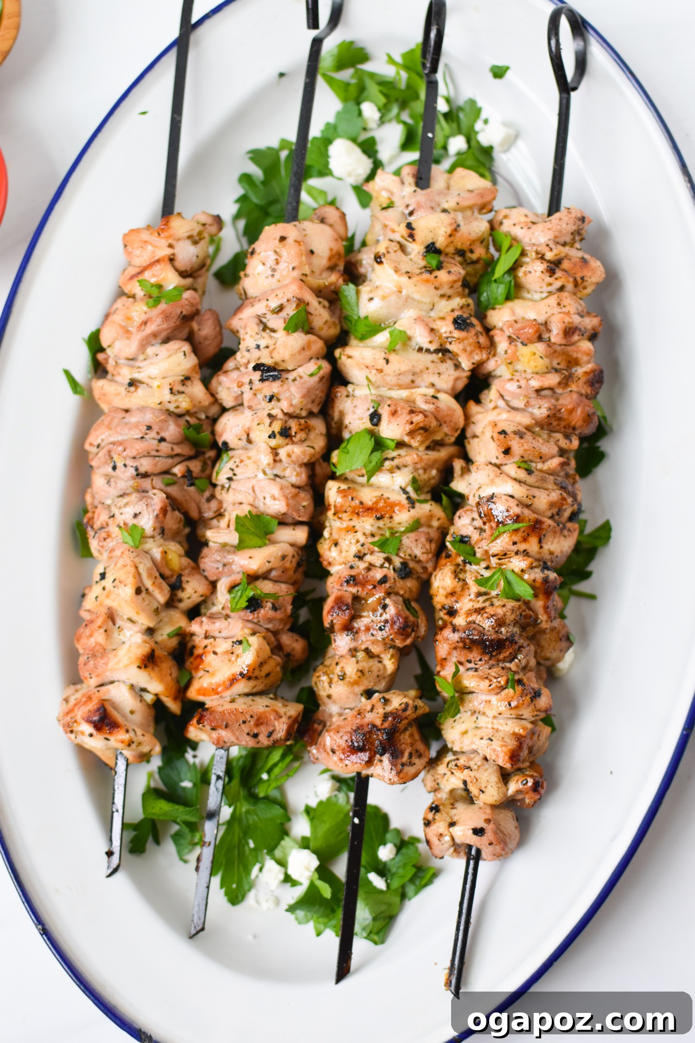 Classic Greek Chicken Souvlaki 2 Grilled Chicken Souvlaki Skewers served on a white platter with fresh herbs.