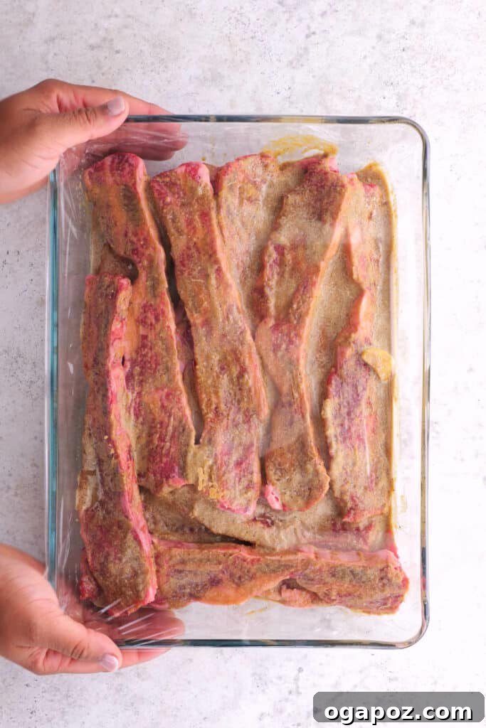 Korean BBQ Galbi 4 Rich, flavorful marinade being poured over thinly sliced beef short ribs in a dish, ensuring every piece is coated.