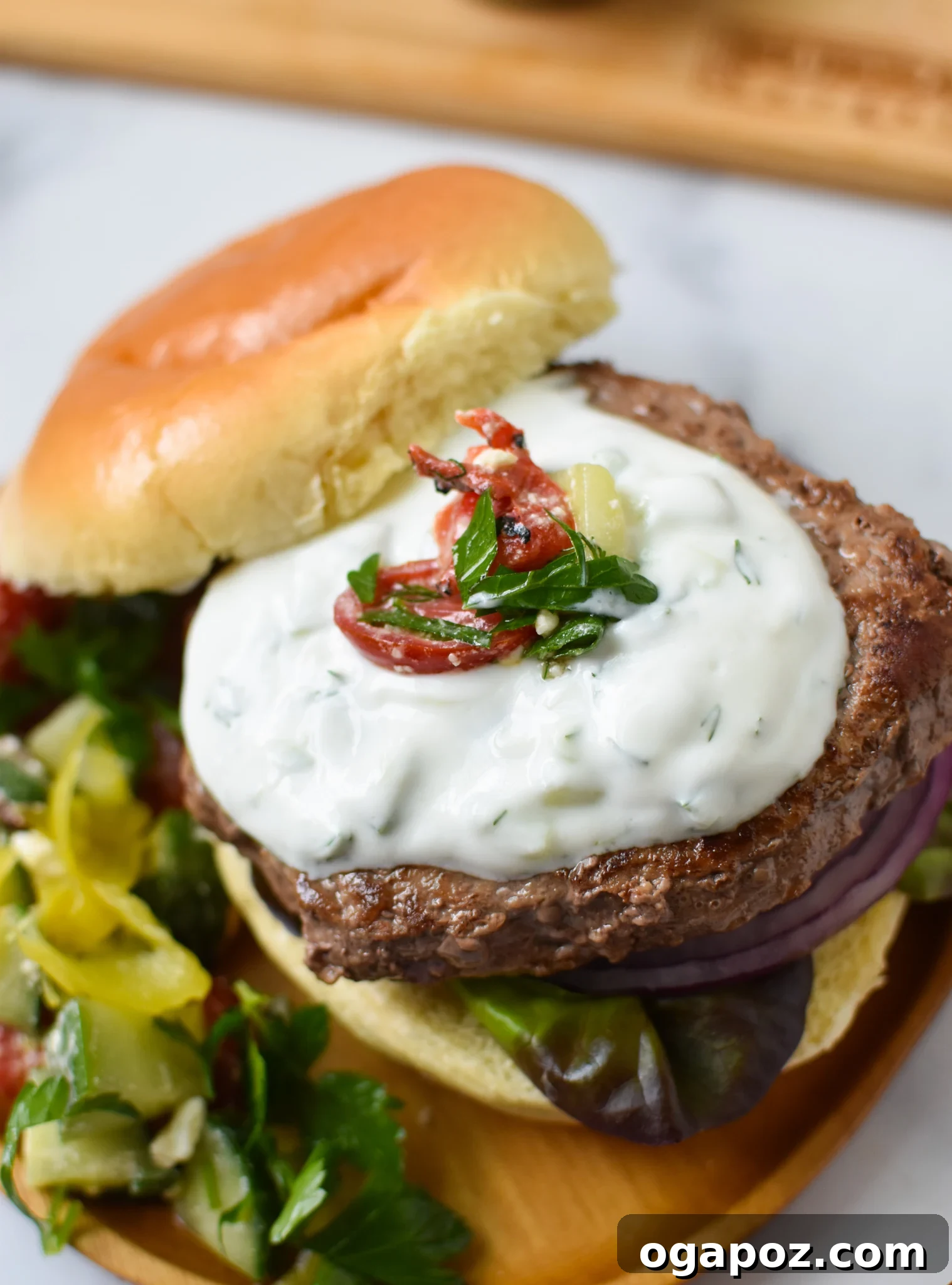 Effortless Greek Burgers 2 Juicy Easy Greek Burger Recipe with creamy tzatziki sauce on a bun.