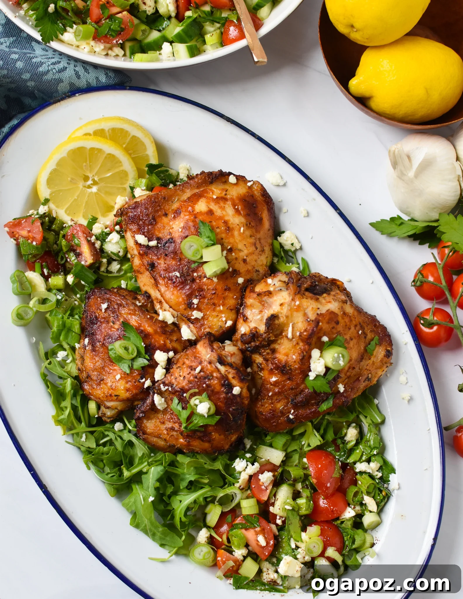 Zesty Mediterranean Air Fryer Chicken Thighs 7 A large white platter filled with Air Fryer Mediterranean Chicken Thighs arranged over a vibrant Mediterranean salad, garnished with herbs.