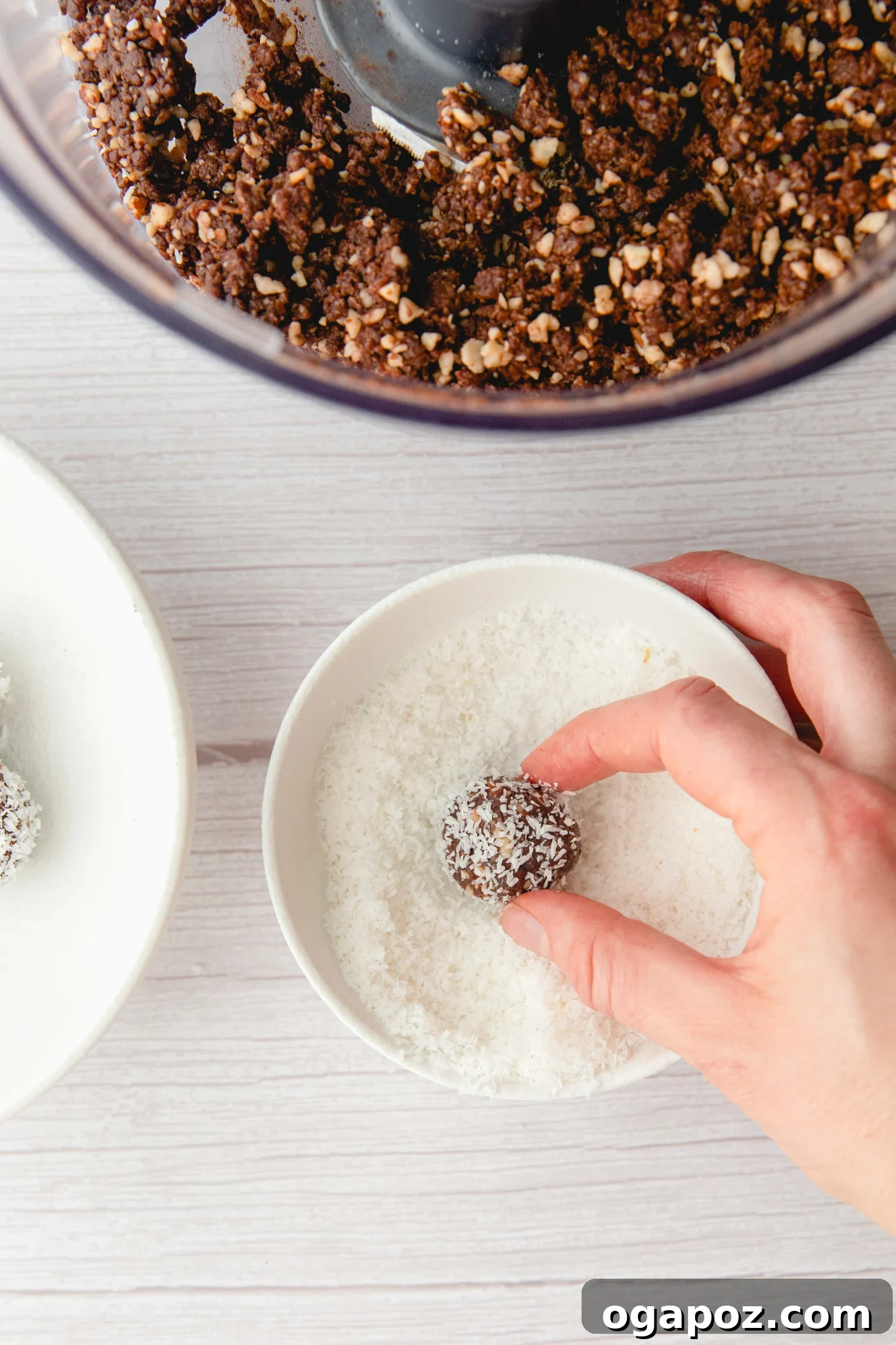 No-Bake Date Energy Bites 8 a hand dipping a date protein ball into a small bowl of desiccated coconut
