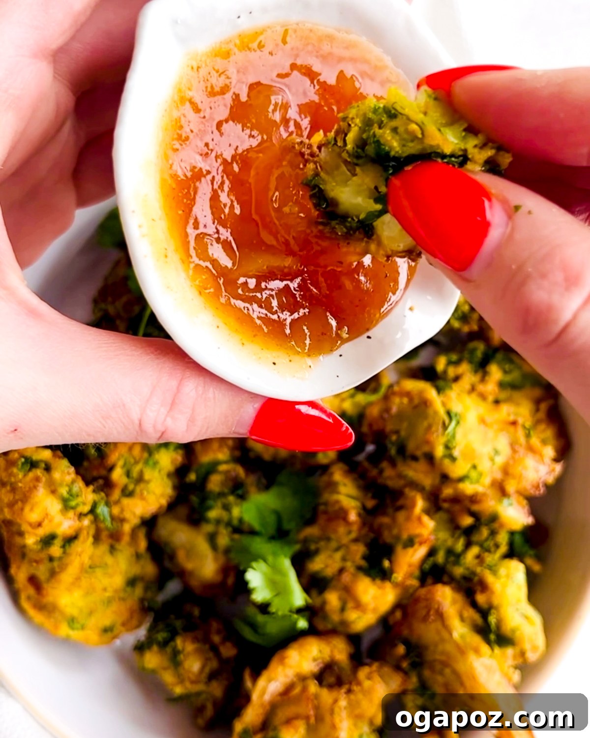 Indian Pakora Effortless Crispy Vegetable Fritters 7 A hand dipping a crispy pakora into a bowl of green mint chutney, illustrating a perfect serving.