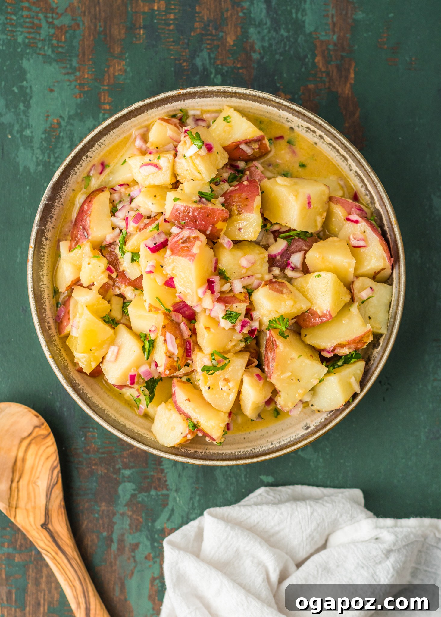 Warm German Potato Salad 7 A wooden spoon scooping a portion of German Potato Salad from a large serving bowl, showcasing its delicious texture and vibrant garnish.