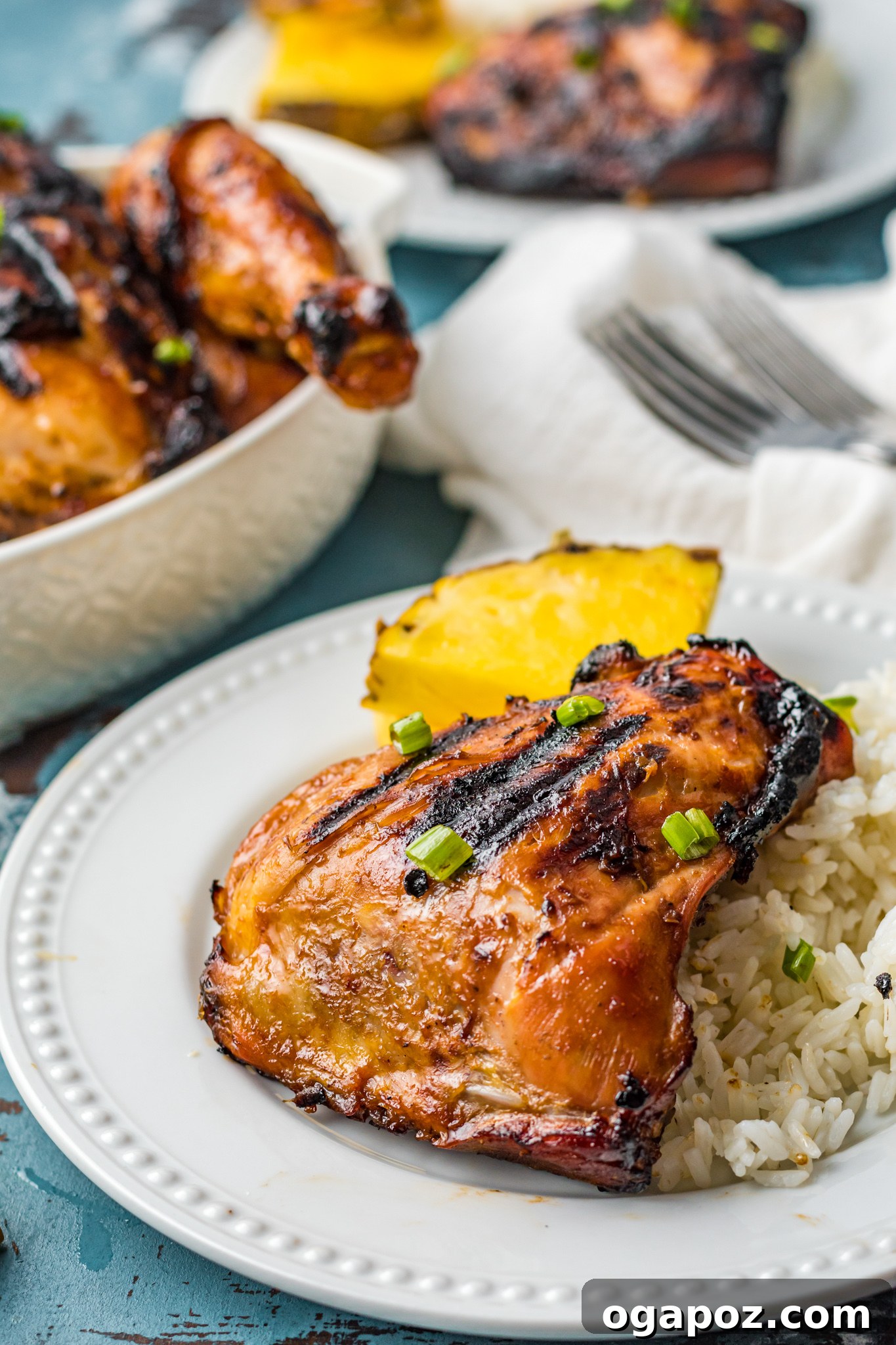 Perfectly grilled Huli Huli Chicken pieces artfully arranged on a pristine white plate, garnished with fresh herbs and a slice of pineapple.