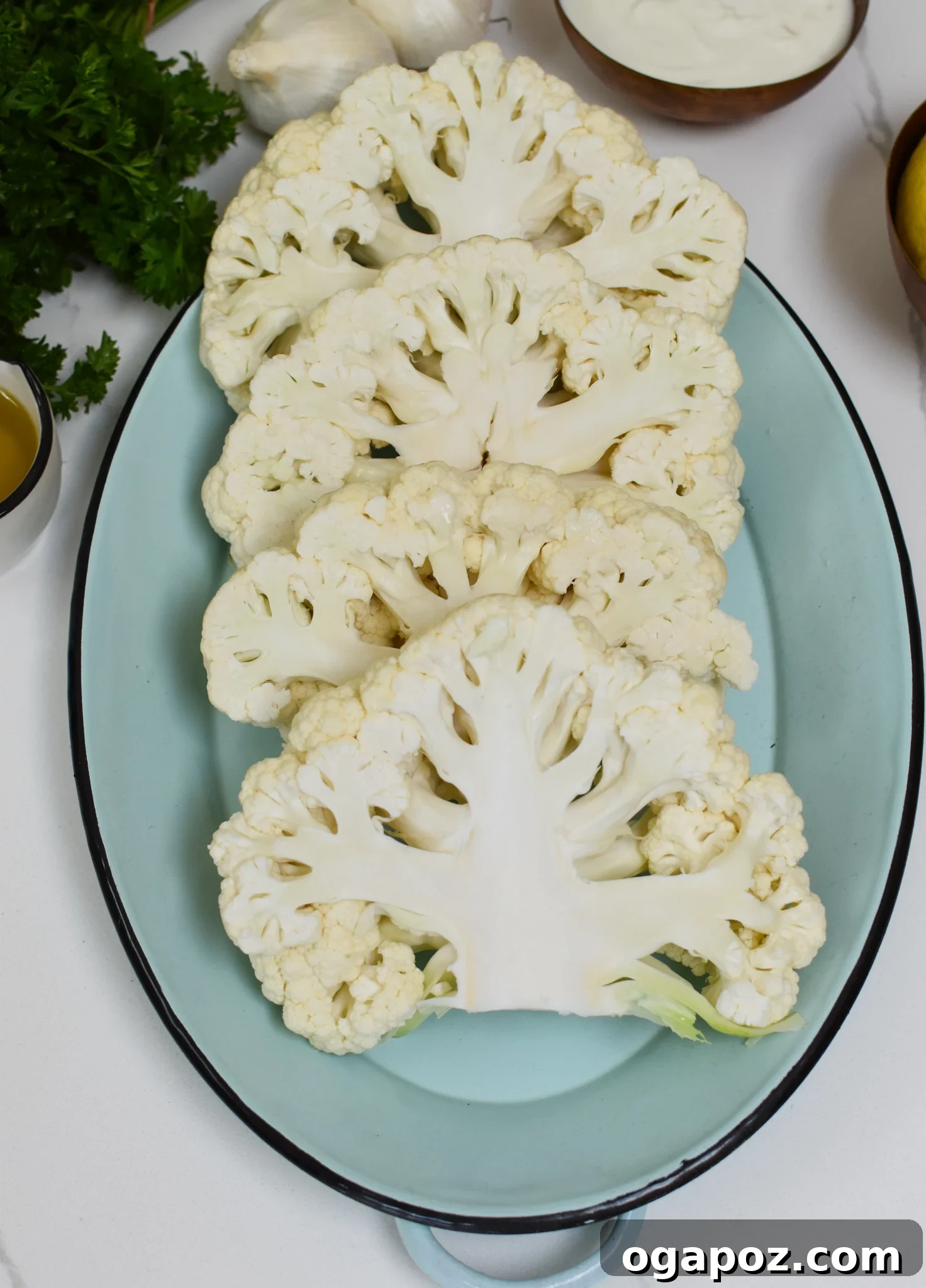 Smoky Grilled Cauliflower Steaks with Creamy Tahini Yogurt 3 Raw cauliflower heads being prepared for grilling, surrounded by fresh lemons and garlic.