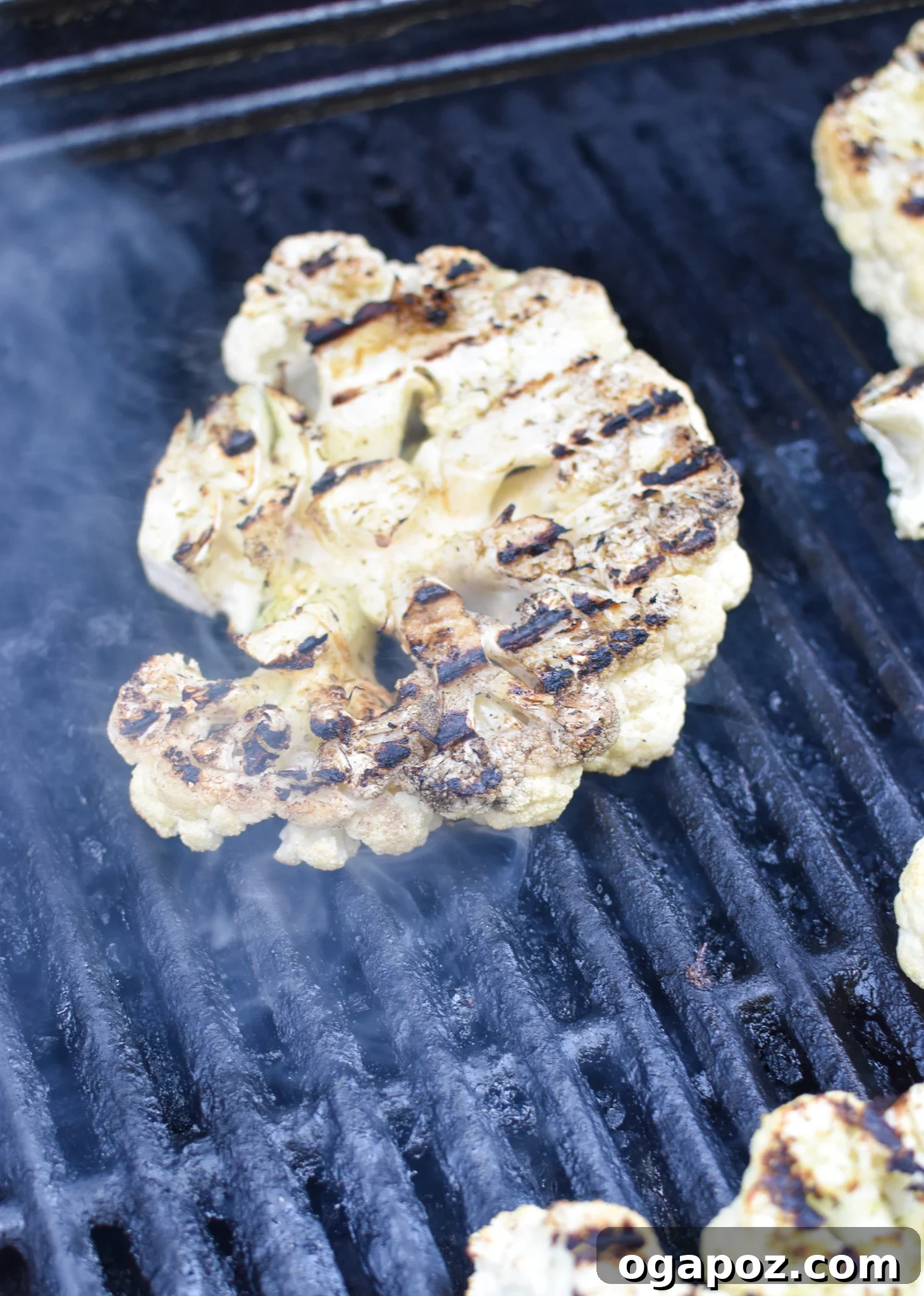 Smoky Grilled Cauliflower Steaks with Creamy Tahini Yogurt 6 Cauliflower steaks sizzling on a hot grill, showing visible char marks.