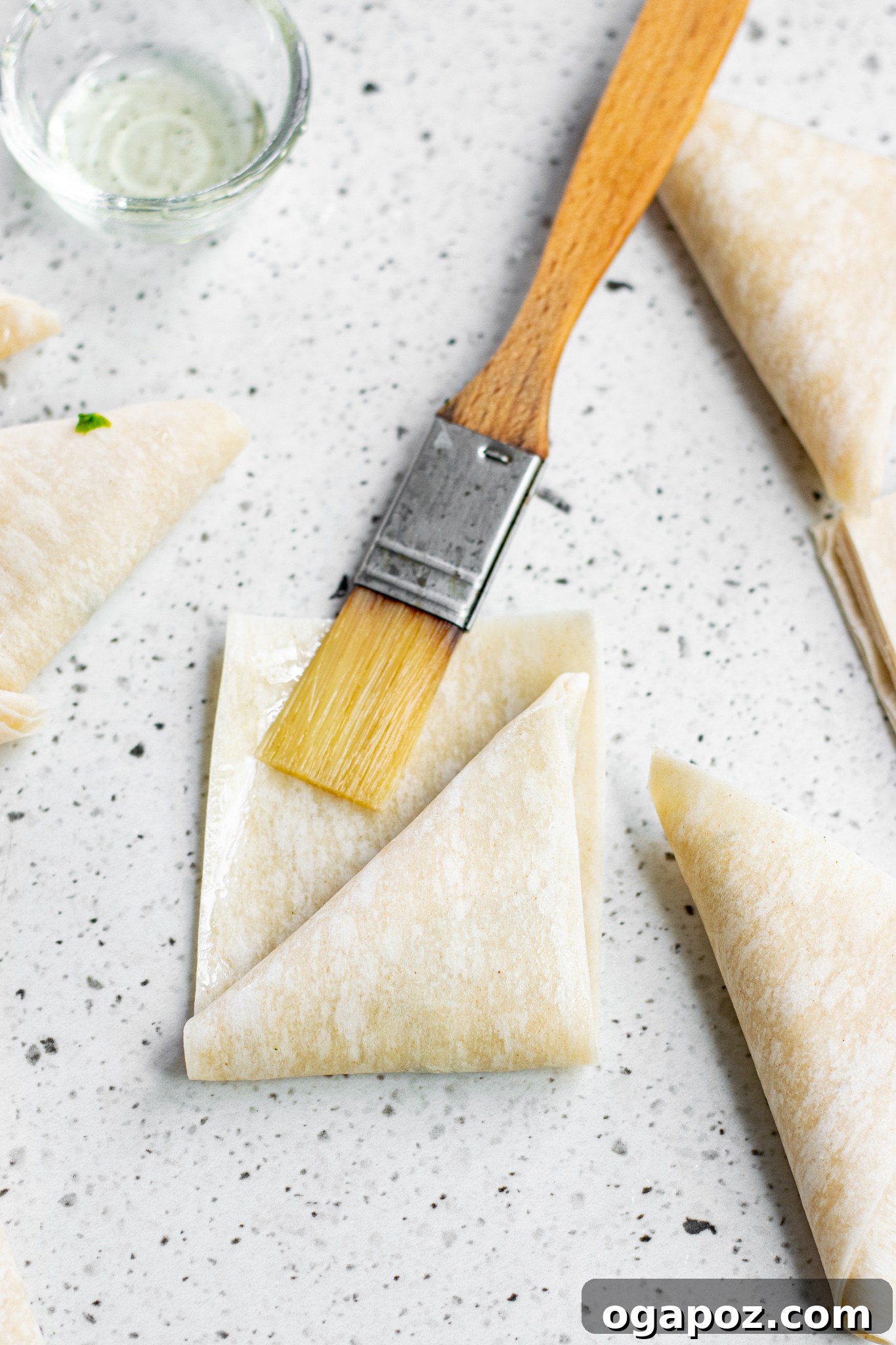 Savory Spinach and Feta Phyllo Pastries 6 Phyllo dough strips being brushed with melted butter.