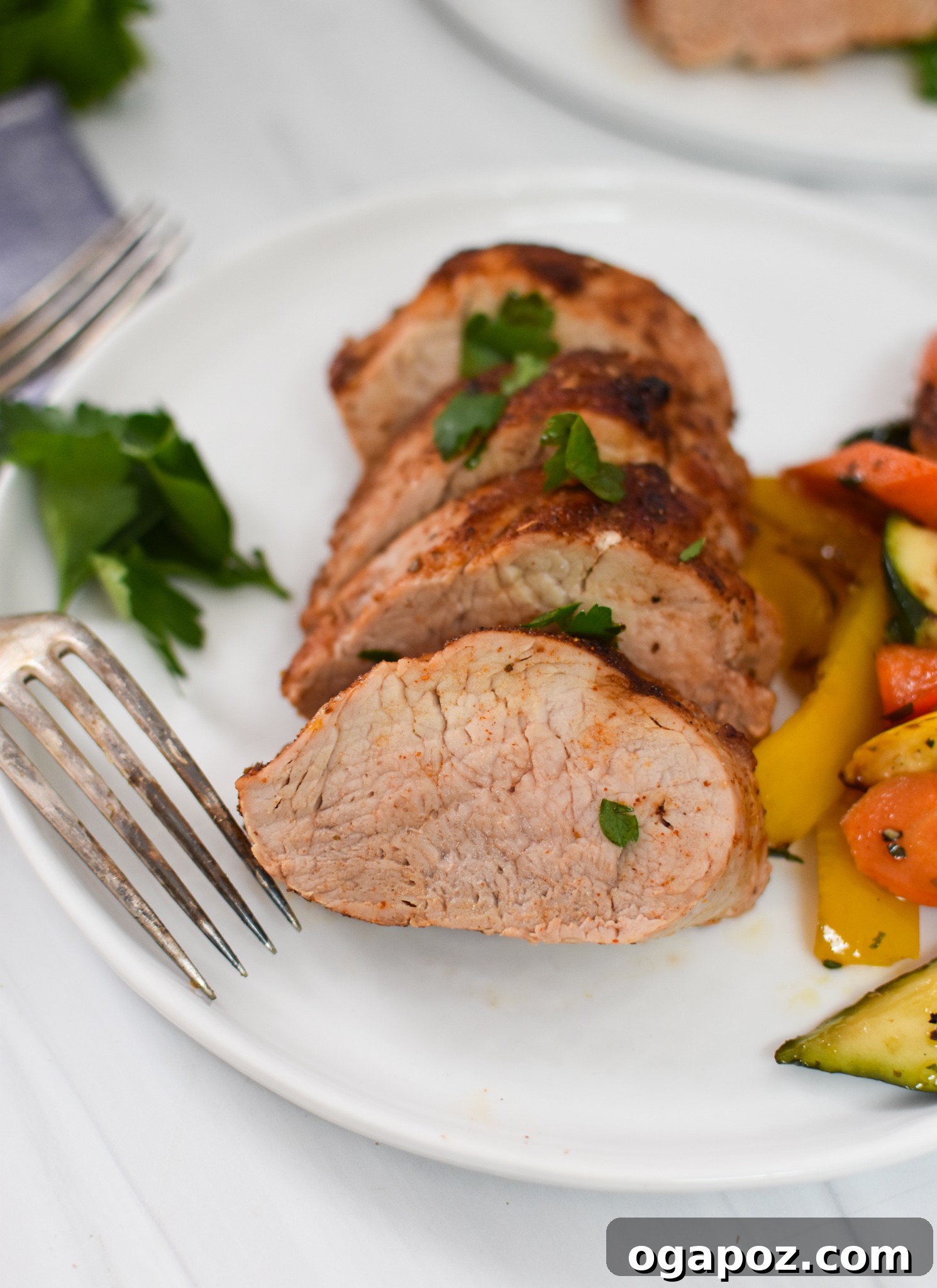 Golden Air Fryer Pork Tenderloin 2 Perfectly cooked Air Fryer Pork Tenderloin sliced on a white plate with a fork, ready to be enjoyed.