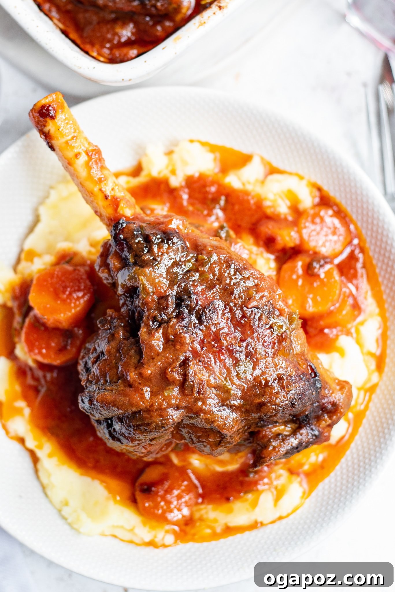 Fall-Off-The-Bone Braised Lamb Shanks 3 Braised Lamb Shanks Recipe with carrots and sauce in a baking dish.
