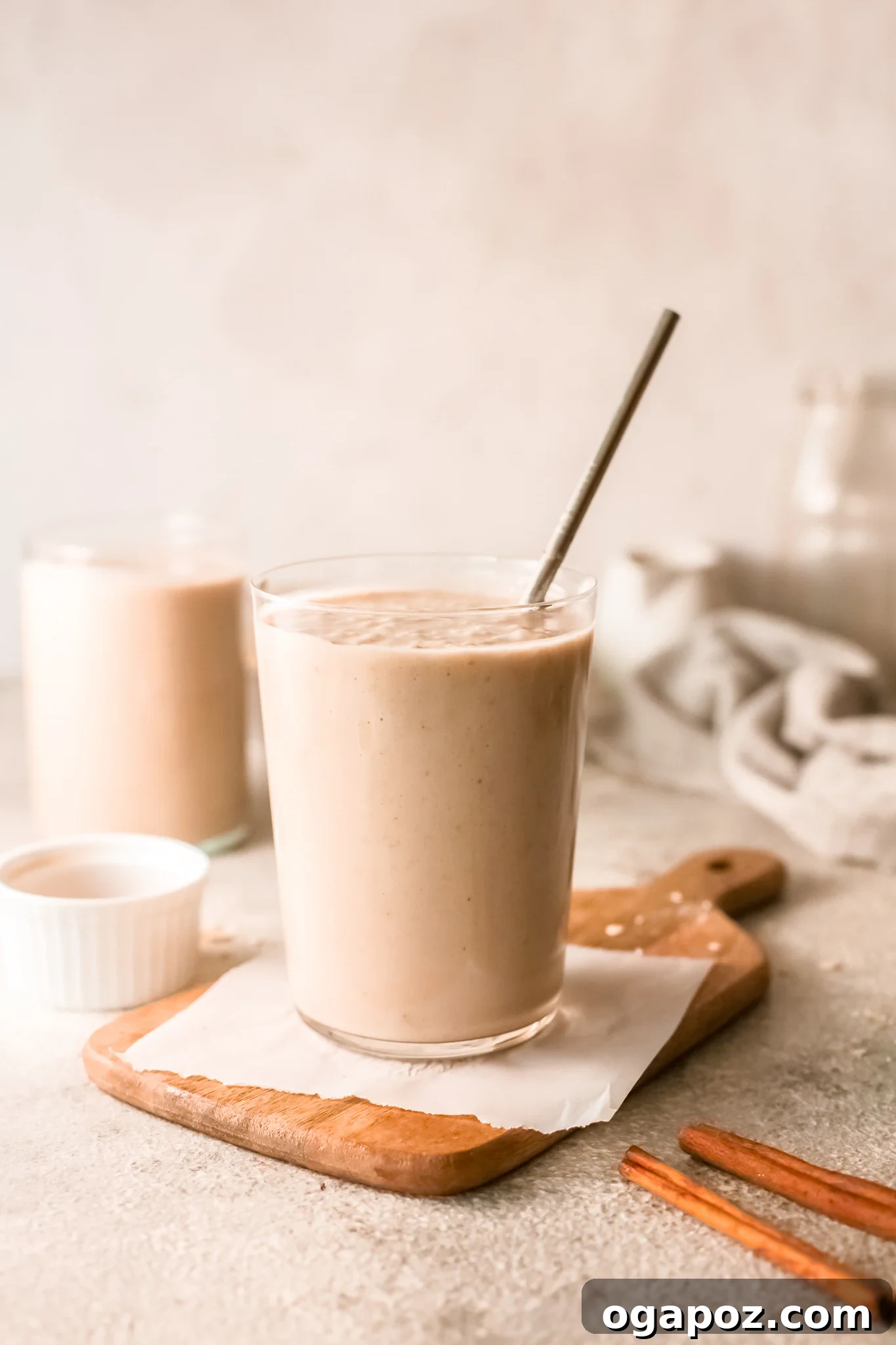 Quick & Healthy Oat Smoothies 2 A tall glass of creamy oat smoothie with a straw, garnished with a sprinkle of cinnamon.