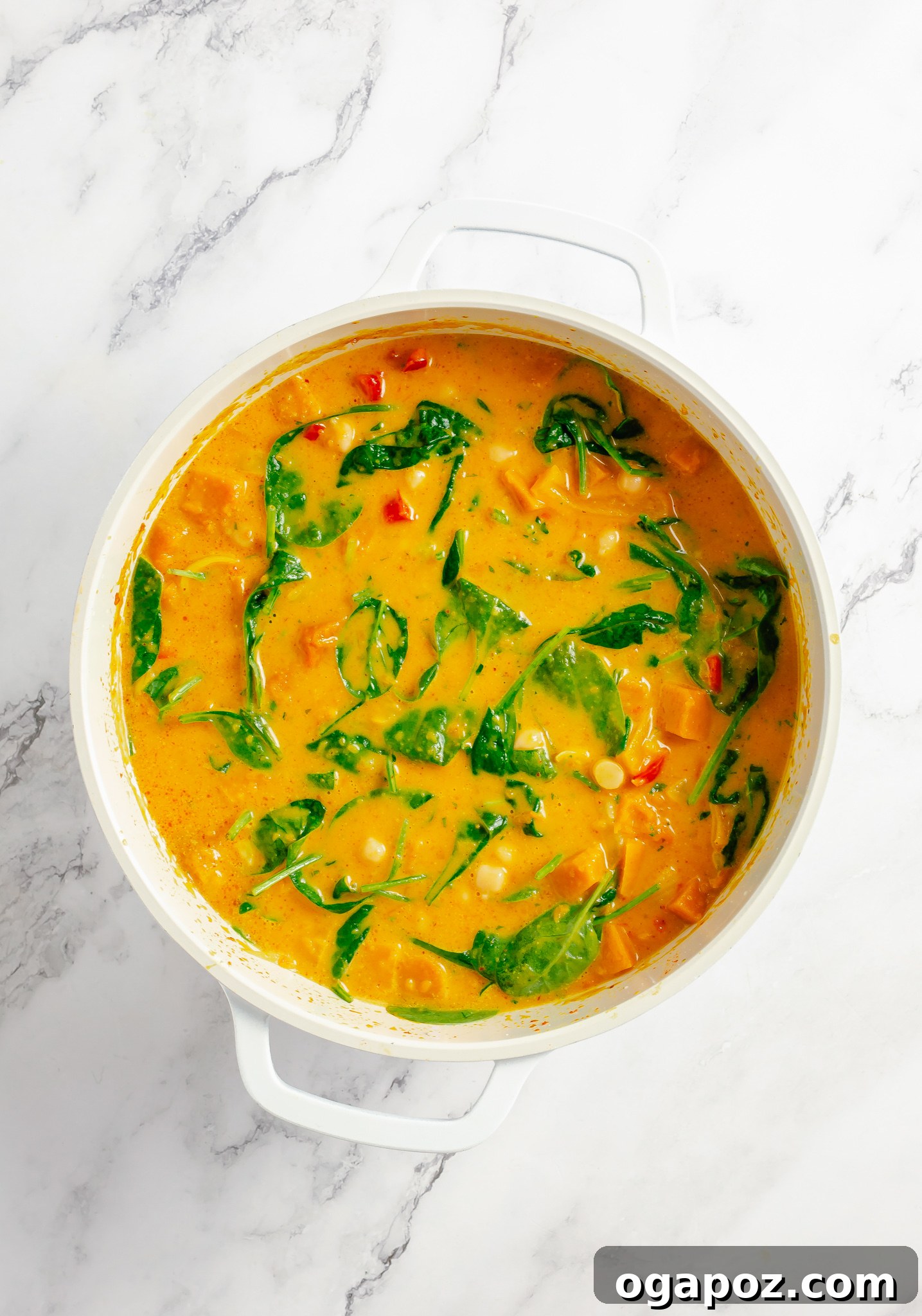 Fresh spinach being stirred into the pumpkin curry in a pot.