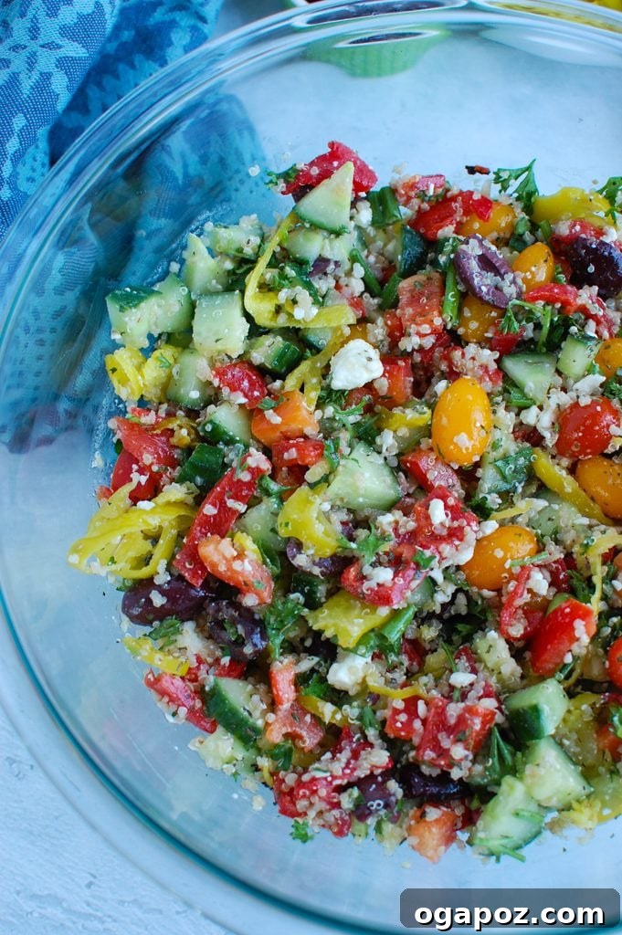 Santorini Sunset Quinoa Salad 3 Close-up of Greek Quinoa Salad in a clear glass bowl, featuring visible ingredients like quinoa, olives, and bell peppers