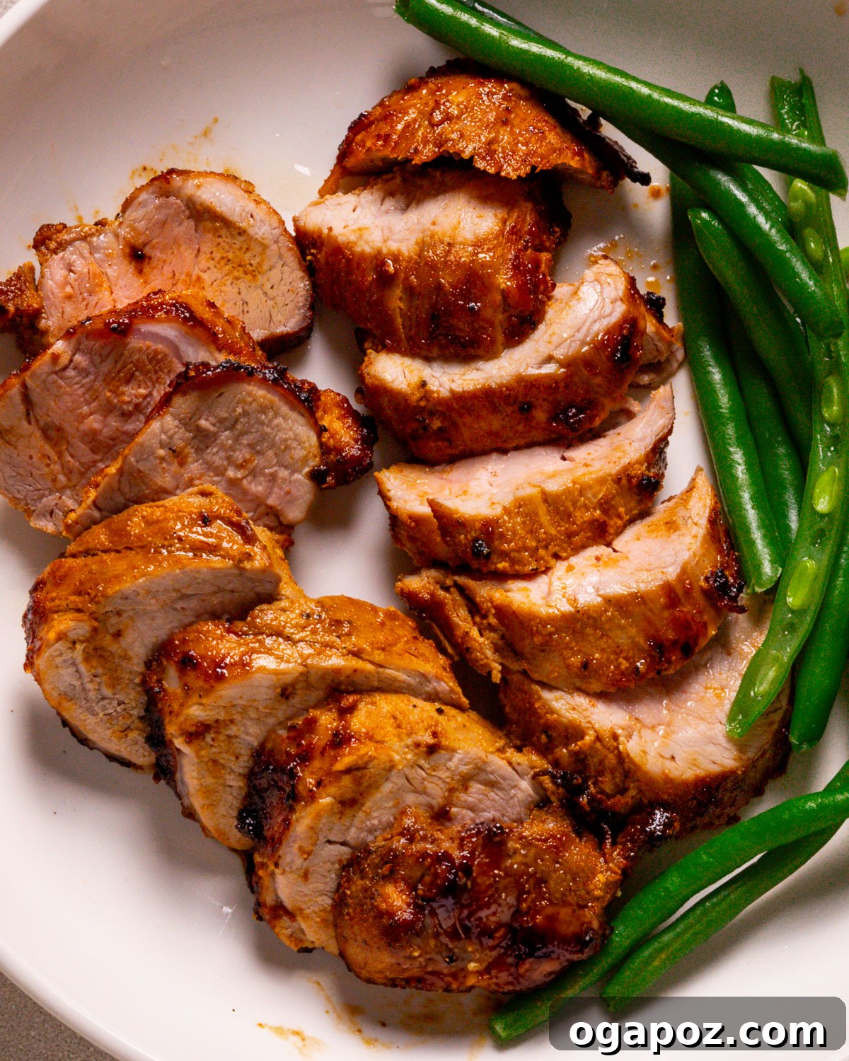 Succulent Air Fried Pork Tenderloin 2 Air fryer pork tenderloin recipe plated with vibrant green beans and a drizzle of sauce, showcasing its tender, juicy interior.
