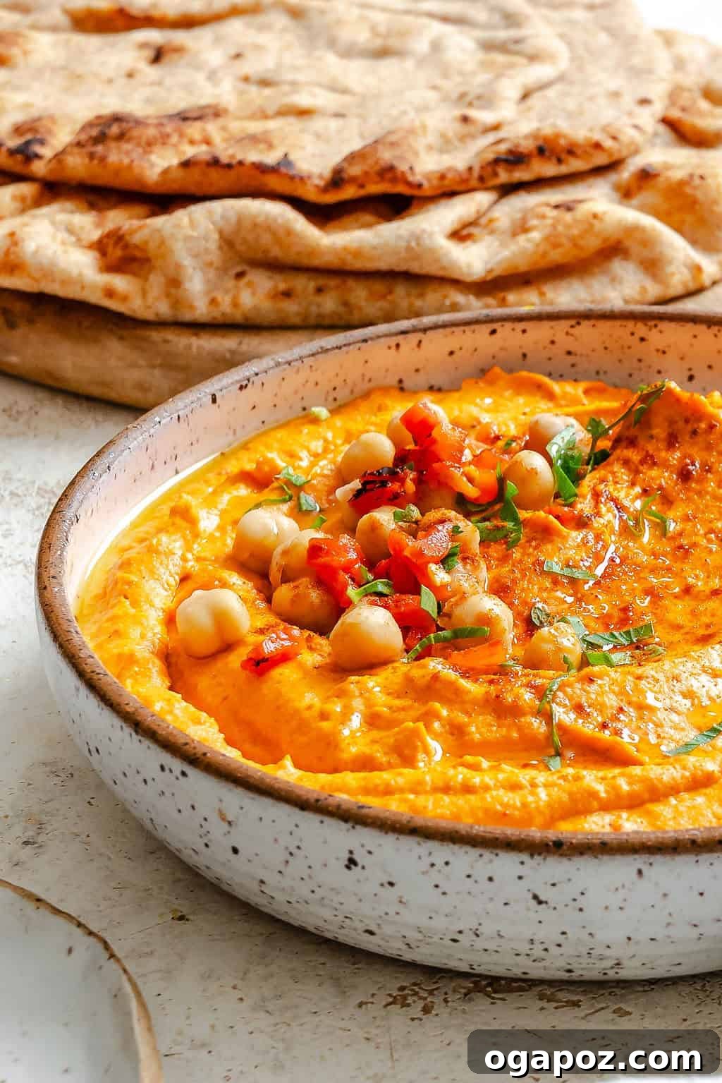 Creamy Roasted Red Pepper Hummus in a white bowl, garnished with olive oil and fresh pita bread