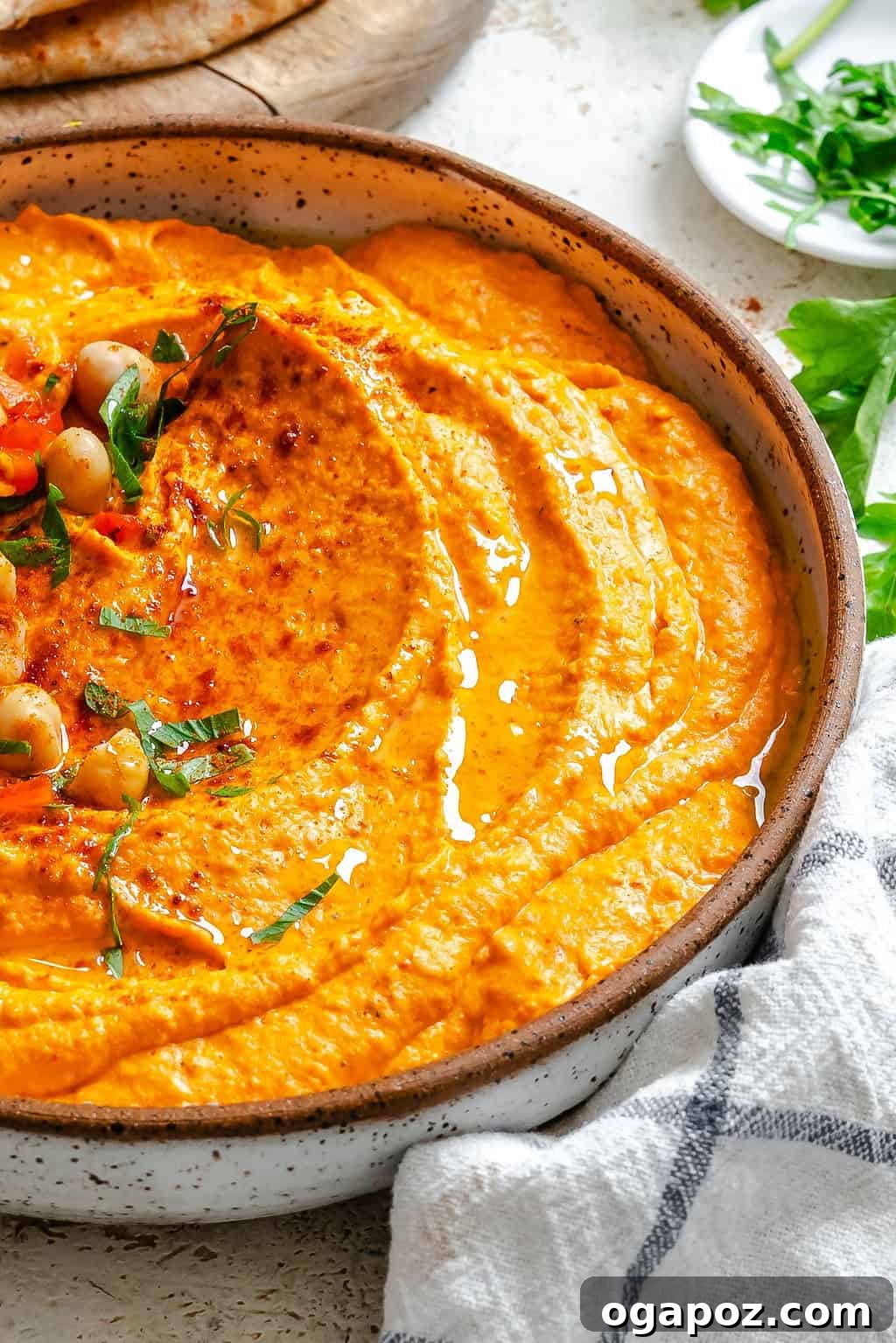 Roasted Red Pepper Hummus garnished with whole chickpeas and fresh parsley in a white bowl