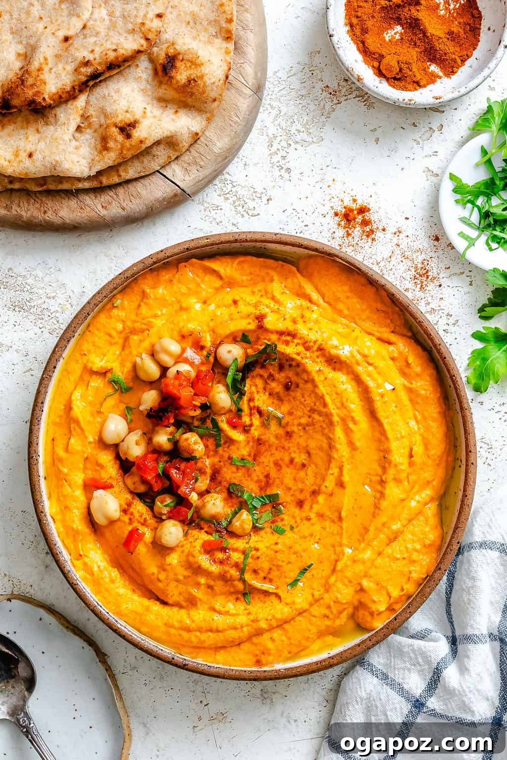 A serving of Roasted Red Pepper Hummus in a bowl, garnished with whole chickpeas and a swirl of olive oil