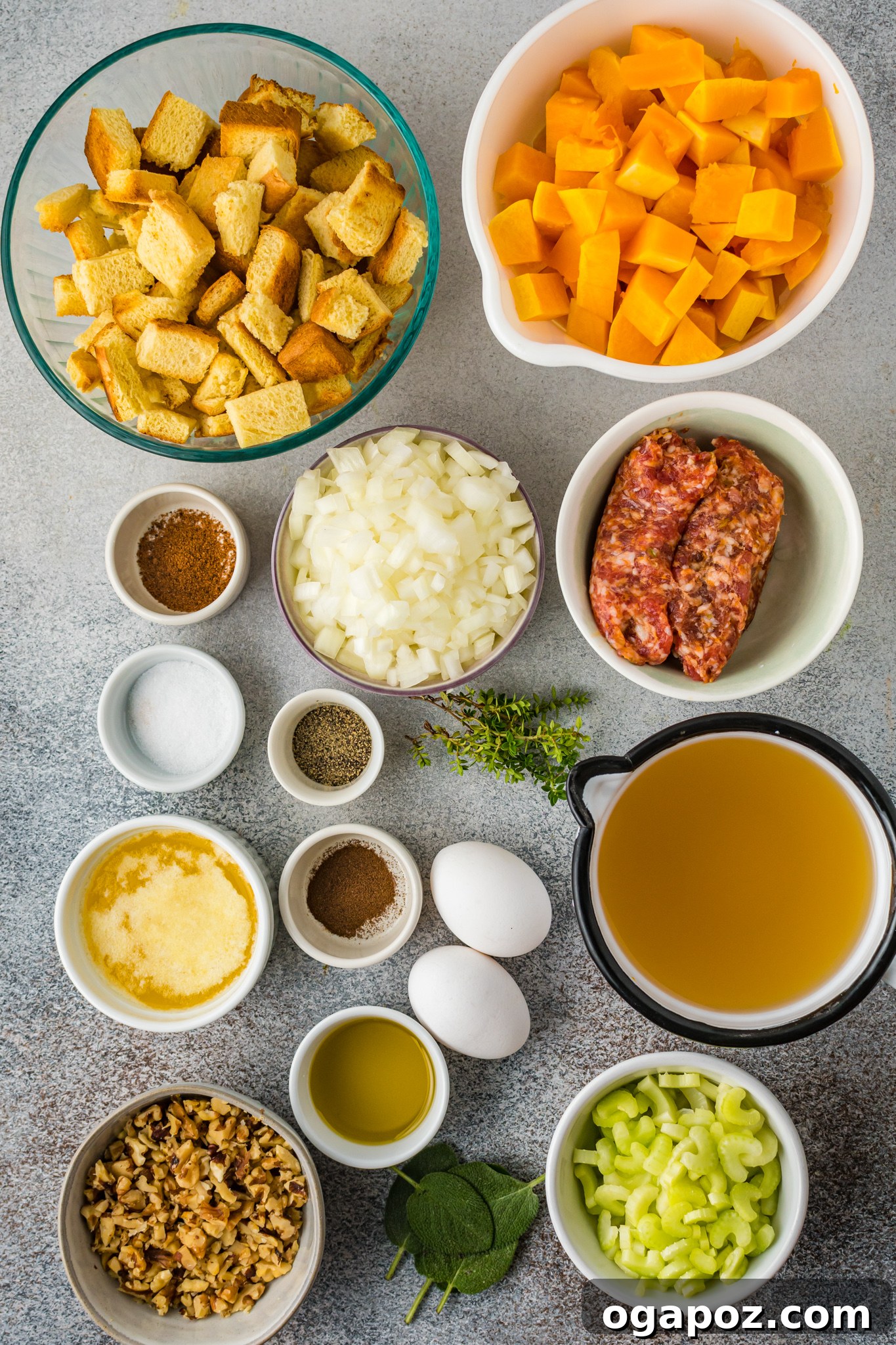 Sweet and Savory Butternut Squash Stuffing 3 A flat lay image displaying all the fresh ingredients for Butternut Squash Stuffing: butternut squash cubes, raw Italian sausage, diced onion, chopped celery, dried Italian bread cubes, butter, nutmeg, allspice, fresh sage, fresh thyme, eggs, chopped pecans, and chicken broth.