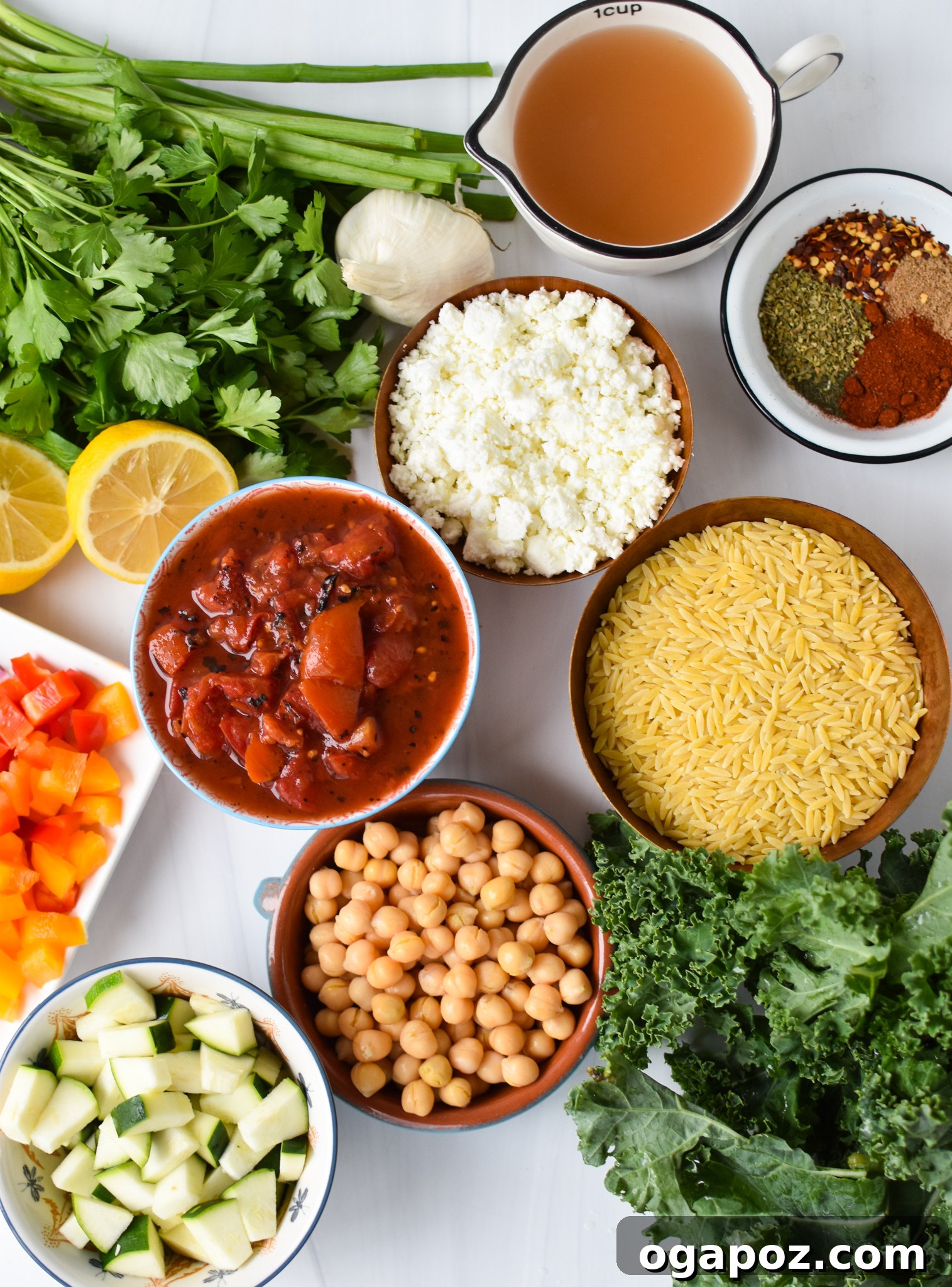 A flat lay of fresh ingredients for Mediterranean Orzo Pasta, including vegetables, spices, orzo, and feta.