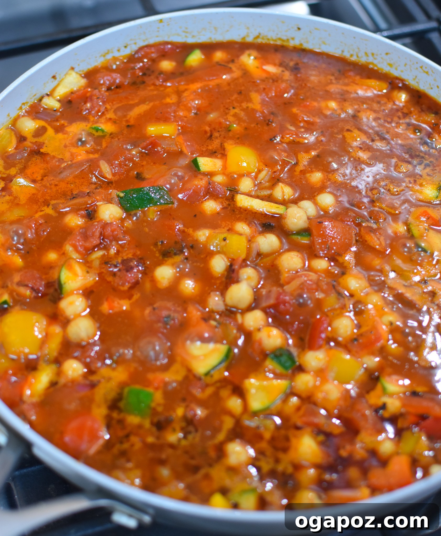 Mediterranean Orzo Pasta simmering gently in a skillet with chickpeas and tomatoes.