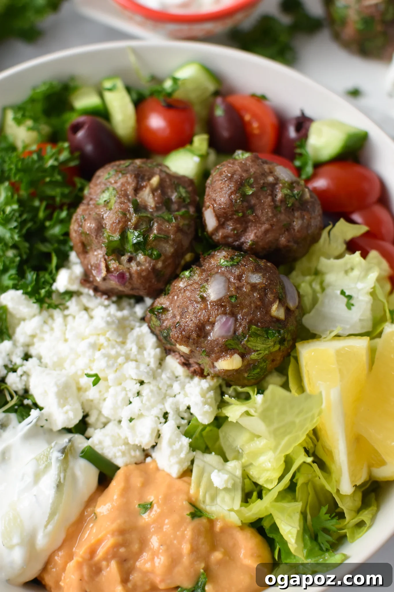 Succulent Mediterranean Baked Beef Meatballs 4 A close-up view of Mediterranean Baked Beef Meatballs nestled in a bed of hummus, garnished with herbs, ready to be enjoyed.