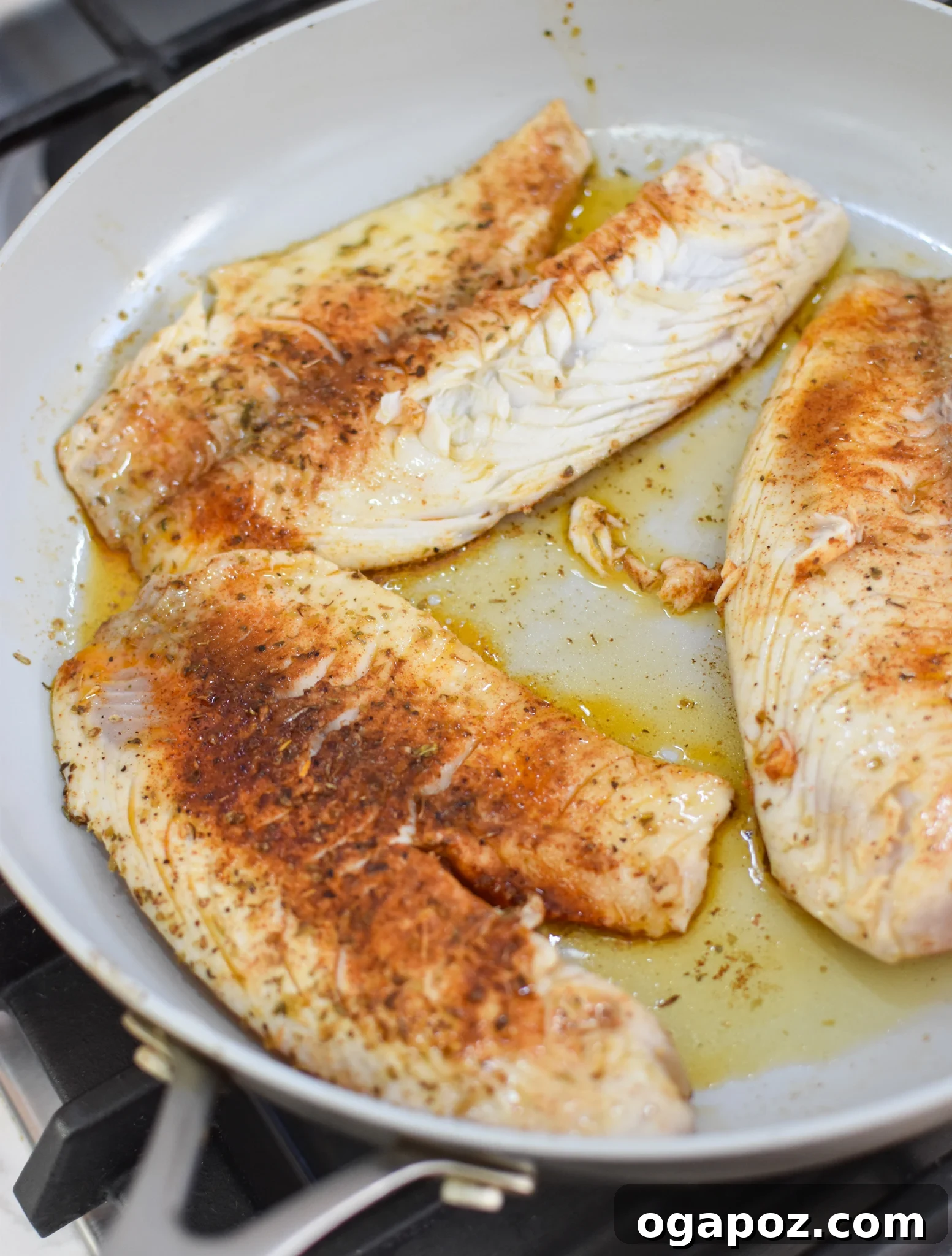 Lemon Herb Greek Tilapia Bake 5 Greek Baked Tilapia fillets searing in a cast-iron skillet.